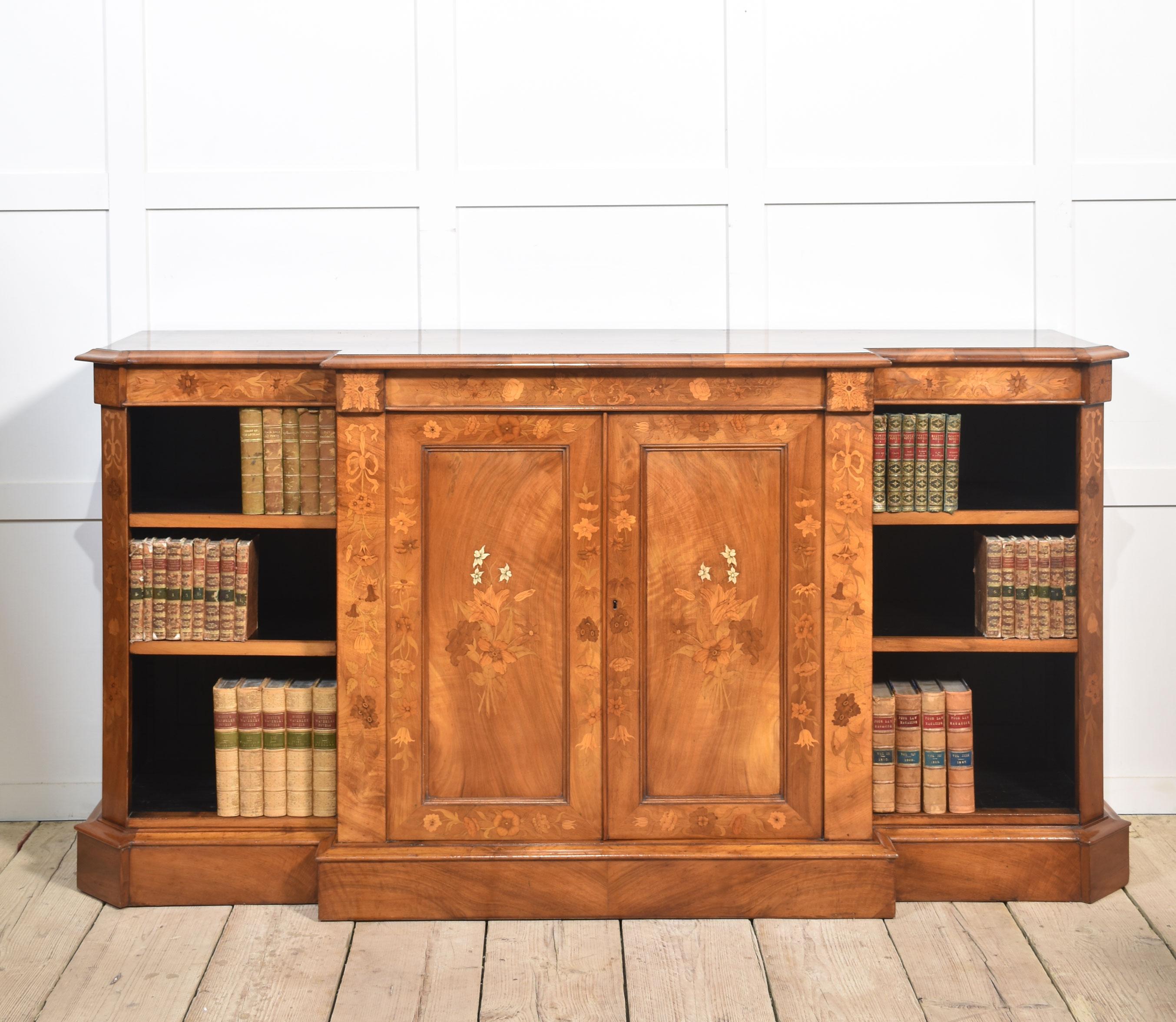 Libreria in legno di noce, con grande piano rettangolare con linee ebanizzate racchiuse da un bordo sagomato e grandi ante centrali con intarsio fogliaceo che si aprono per rivelare l'interno a ripiani. Sfogliato da librerie aperte regolabili. Il