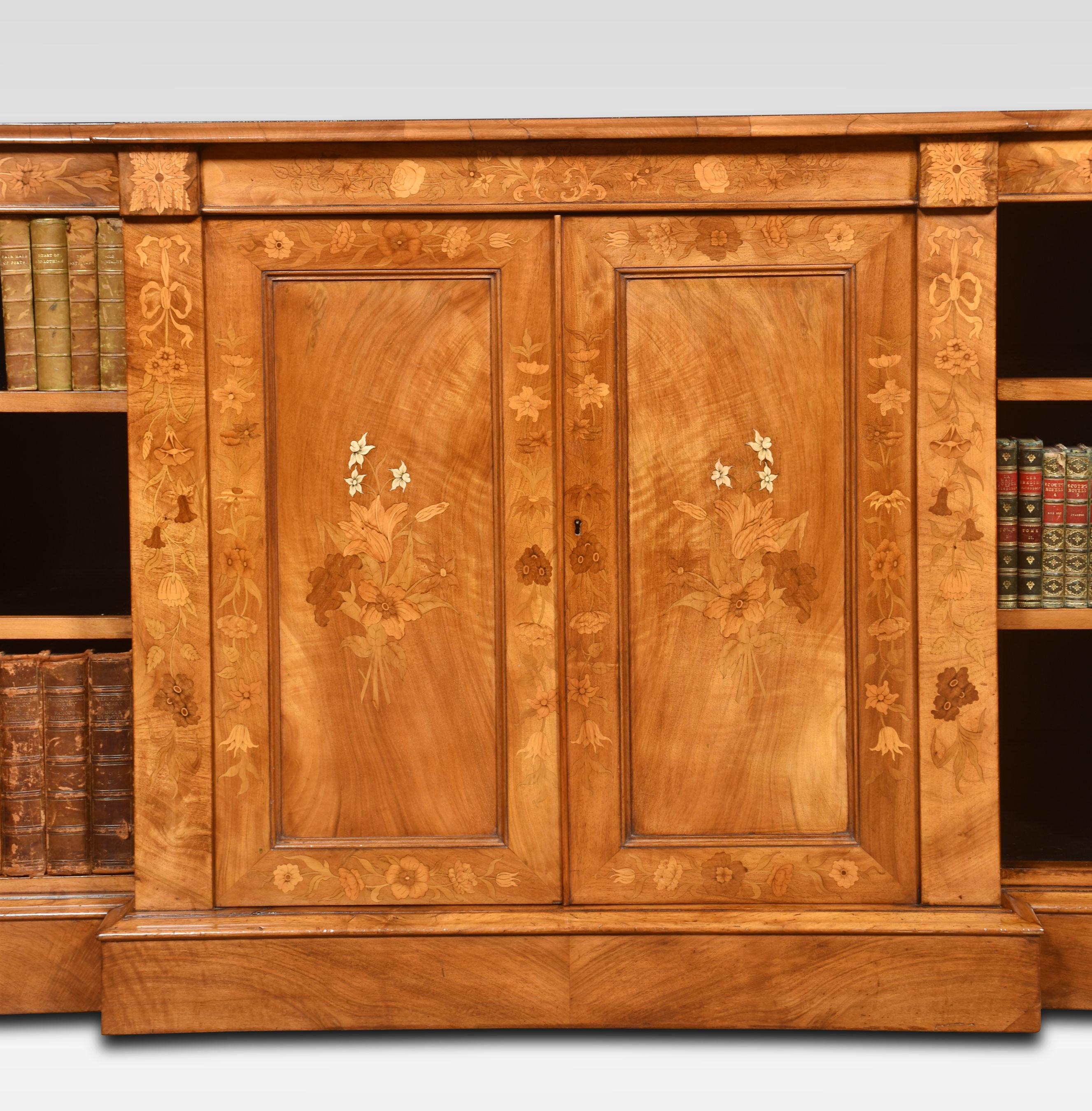 Walnut bookcase, the large rectangular breakfront top with ebonised line detail enclosed by moulded edge. to the large central panelled doors with foliated inlay opening to reveal shelved interior. Flaked by adjustable open bookshelves. All raised
