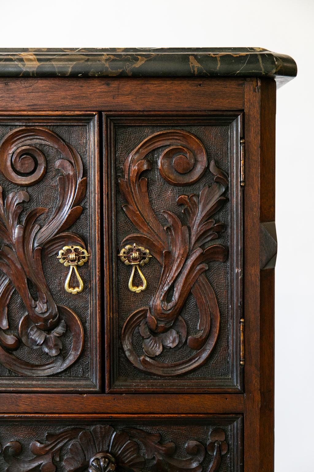 Walnut lingerie cabinet has a black and gold marble top. The drawer front and doors have carved floral arabesques, and the drawers have the original mushroom carved knobs. The base terminates in four carved cabriole legs.