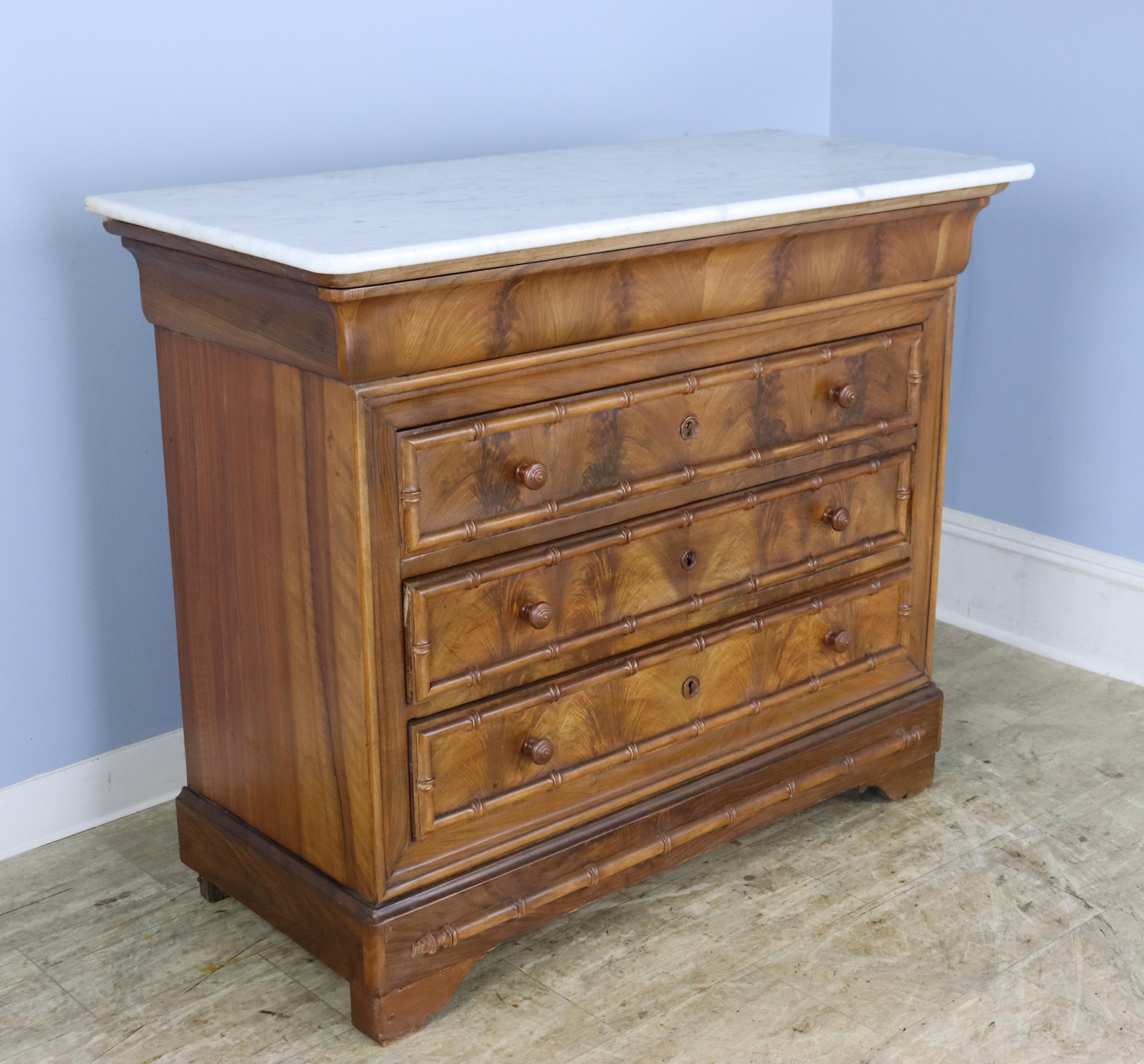 A French chest of drawers in the Louis Philippe style with faux bamboo trim and mouldings, with spectacular walnut grain. Drawers run nicely.  Marble is in good antique condition with some small chips and areas of wear.  Heavy and sturdy.