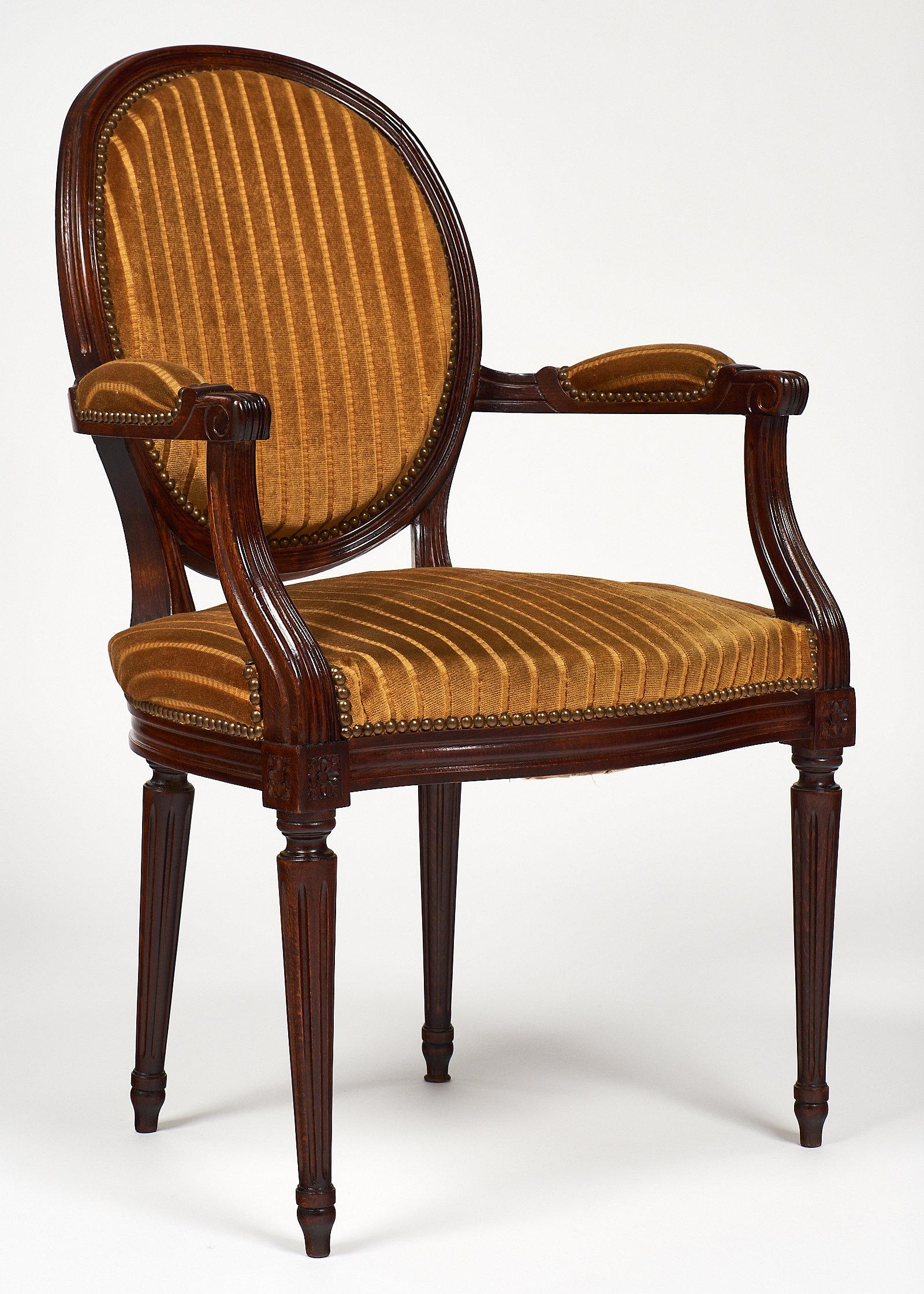 Louis XVI style walnut armchair with tapered legs and medallion back. We love the hand-carved details throughout. The original stamped velvet upholstery is in decent condition, with decorative brass nailheads.