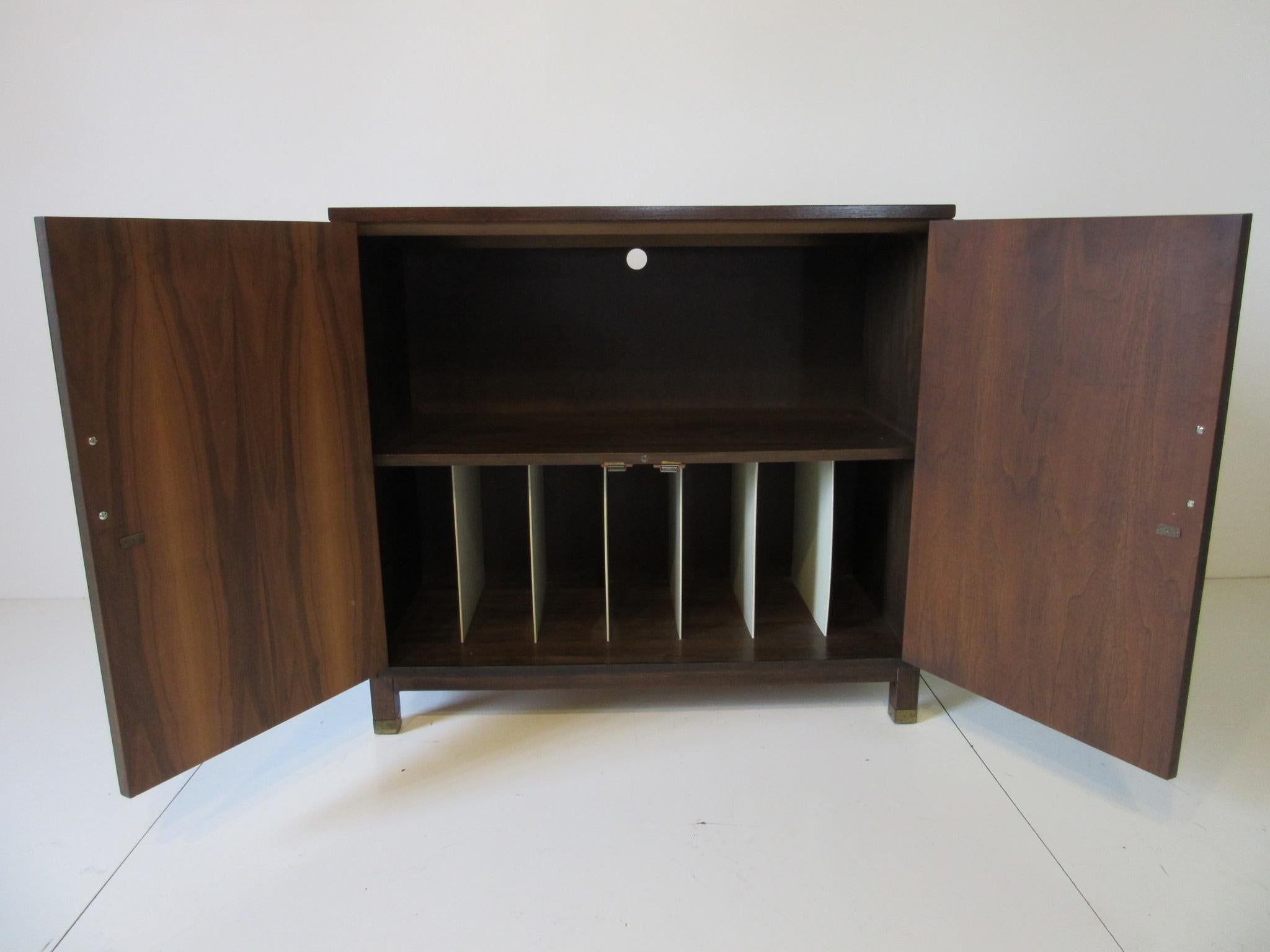 A dark walnut two door media cabinet with the upper area for stereo or other equipment , has a pre-drilled hole for cords and the lower area has dividers for your LP records. The handles to the doors are brass as are the bottom leg caps, this piece