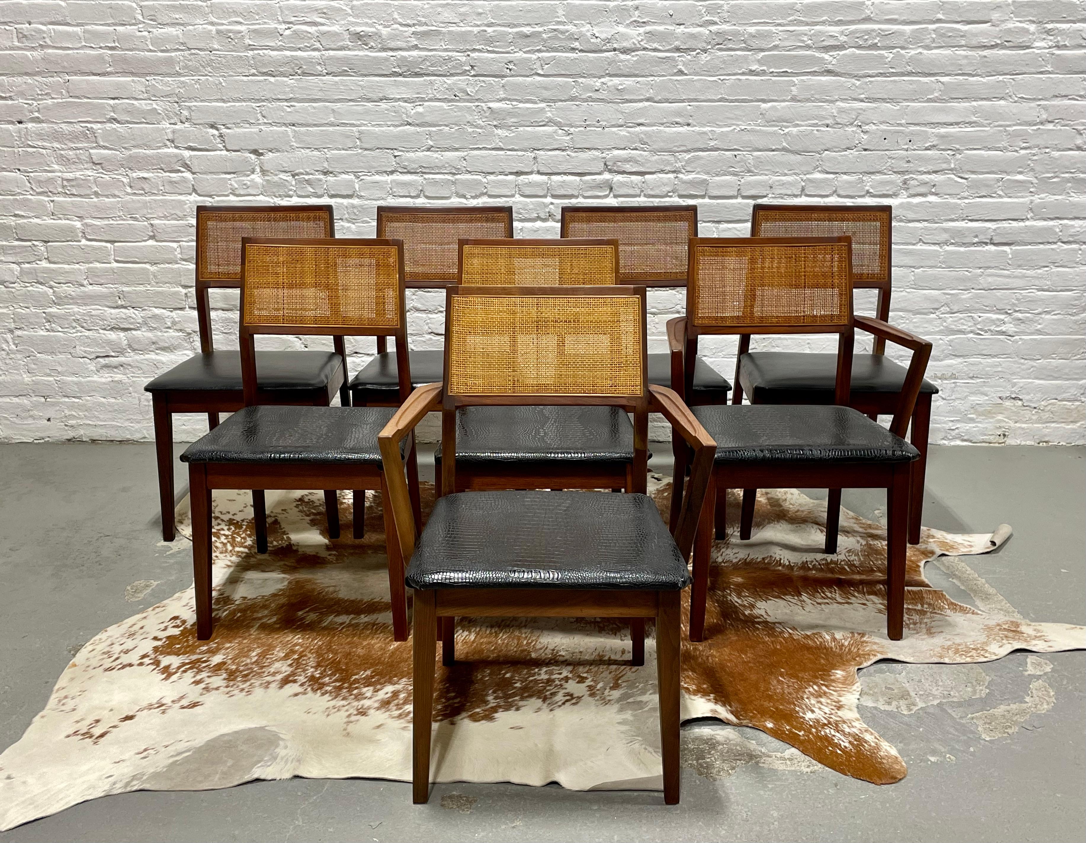 Set of EIGHT Mid Century Modern Walnut Caned Dining Chairs, c. 1960's. Lovely solid frames with incredible wood coloring and caned back rests. Upholstery is a simple black naugahyde on 4 of the chairs and a faux black lizard skin on the armchairs