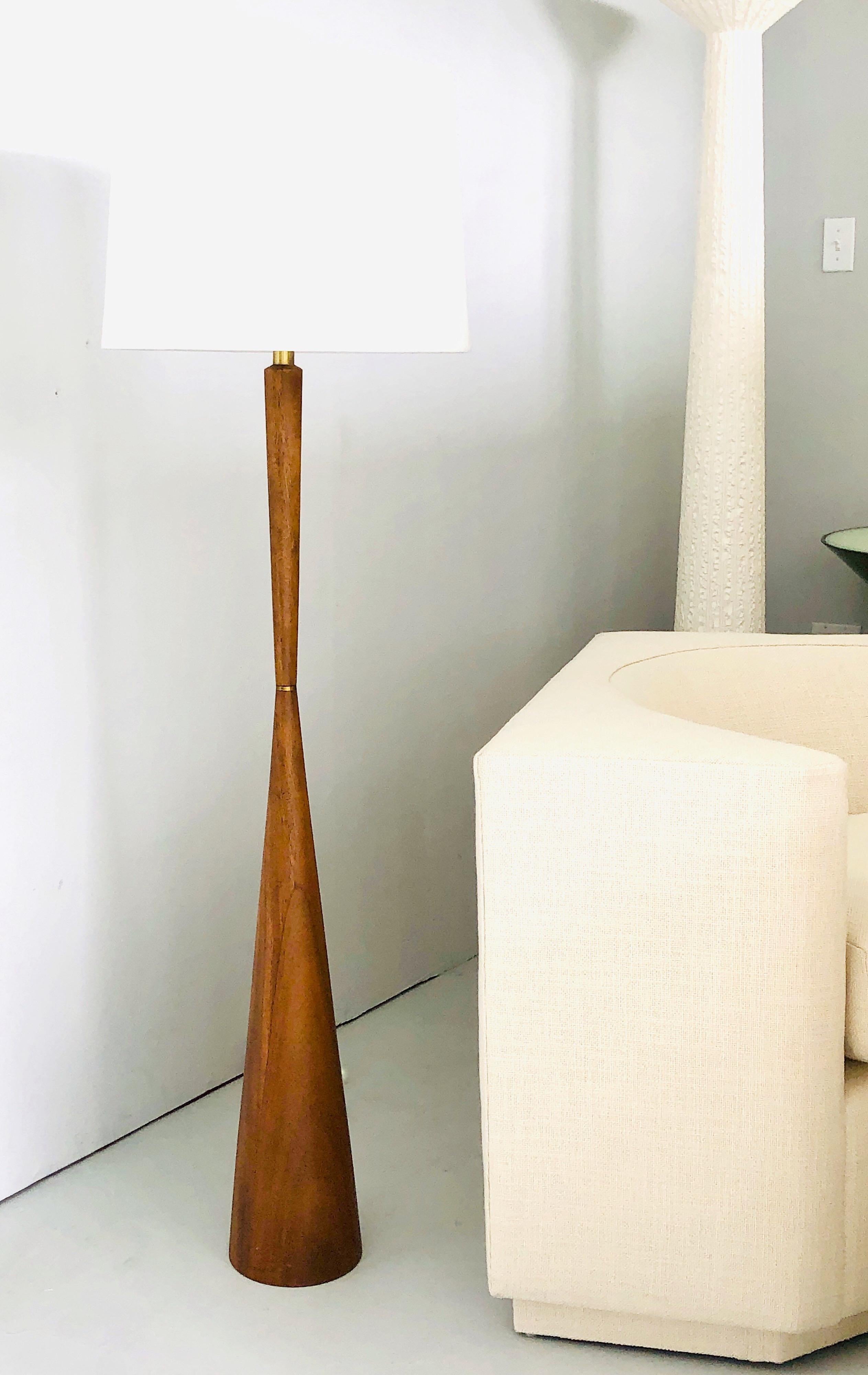 A Modernist slender hourglass floor lamp. It is walnut with a brass ring at the waist.