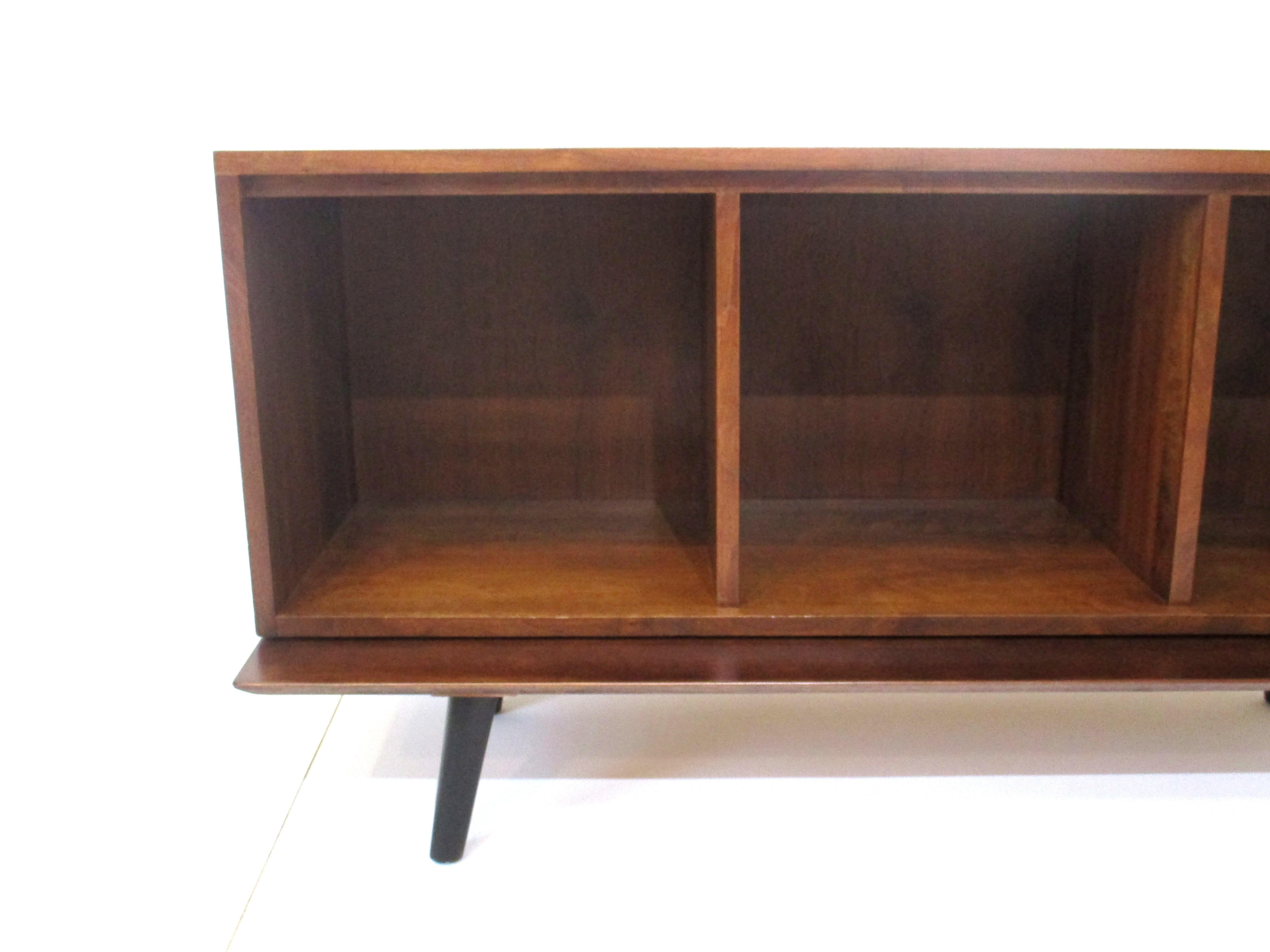 A walnut cabinet with three open box sections for records sitting on a platform bench with conical legs . The cabinet will hold quite a few records and you can use the top for your reciever and turntable designed in the manner of Paul McCobb . Items
