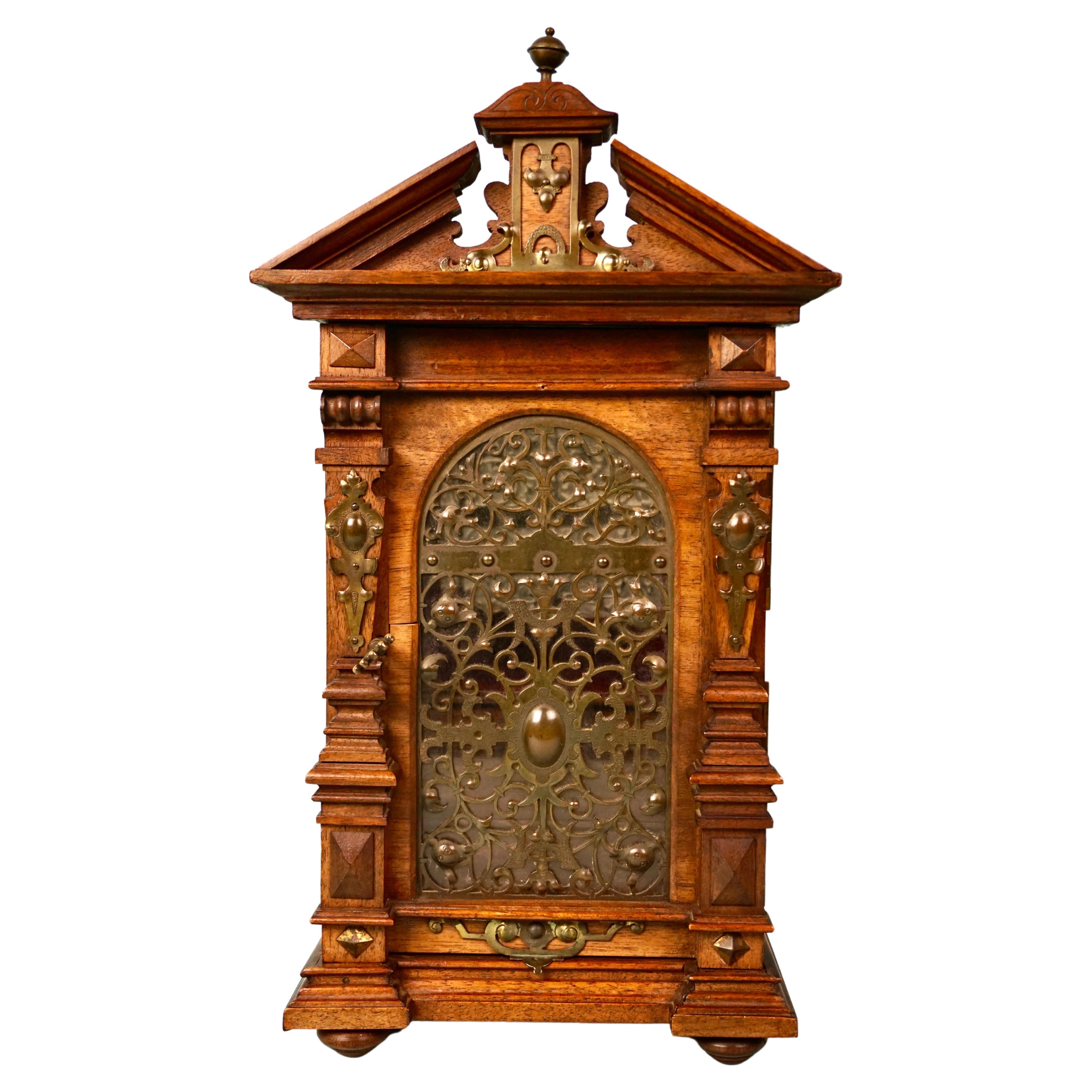 A very well-detailed figured walnut table cabinet in the neoclassical taste with an elaborate metal filigree door opening to reveal a beveled mirror above 2 small drawers, surmounted by a broken pediment cornice centered by a finial. The piece rests