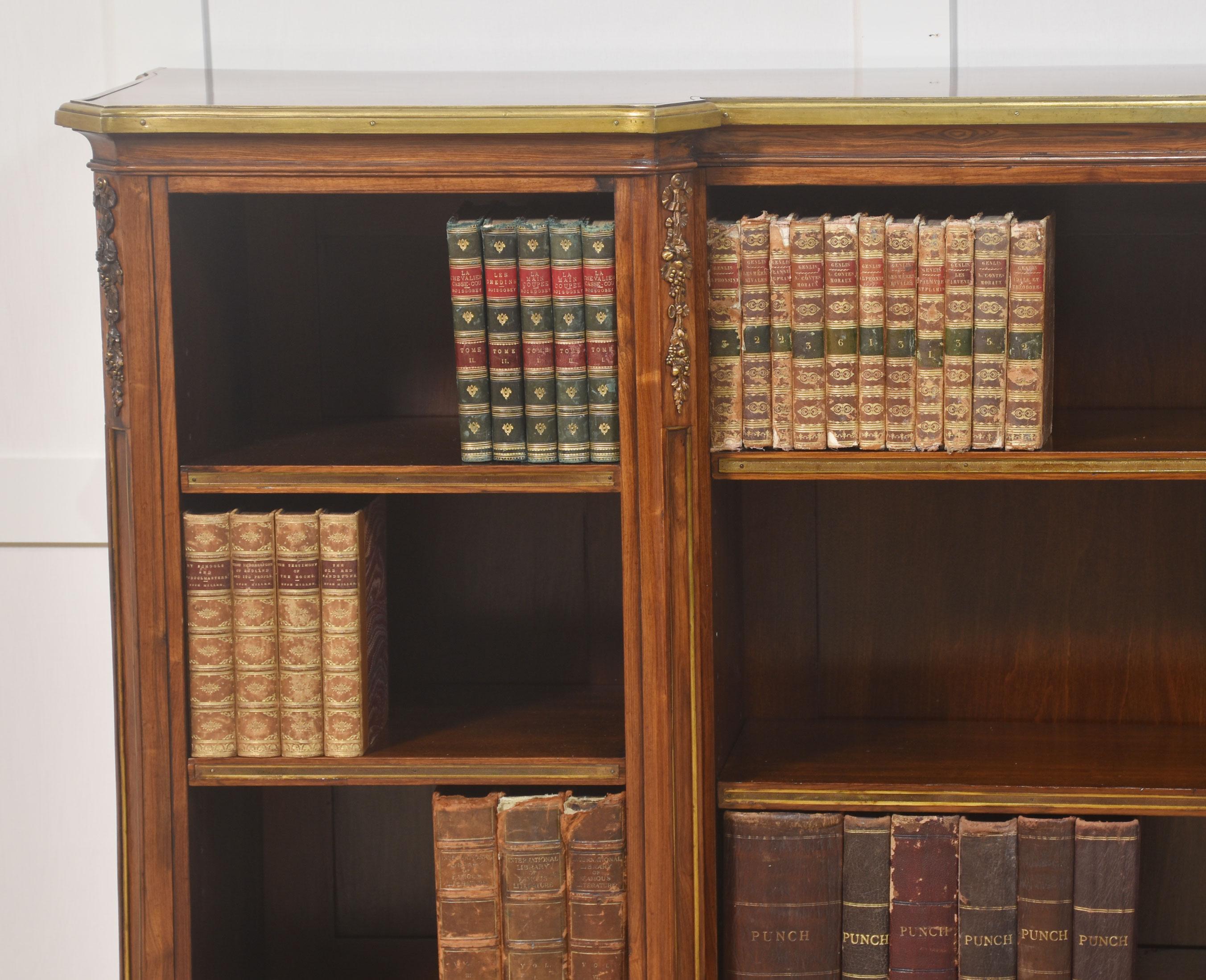 Kingwood ormolu mounted open bookcase, the well-figured inverted breakfront top enclosed by brass banding. The bookshelf is fitted with three bays of ajusable shelves having decrative ormolu mounted, canted columns. All raised on five decorative