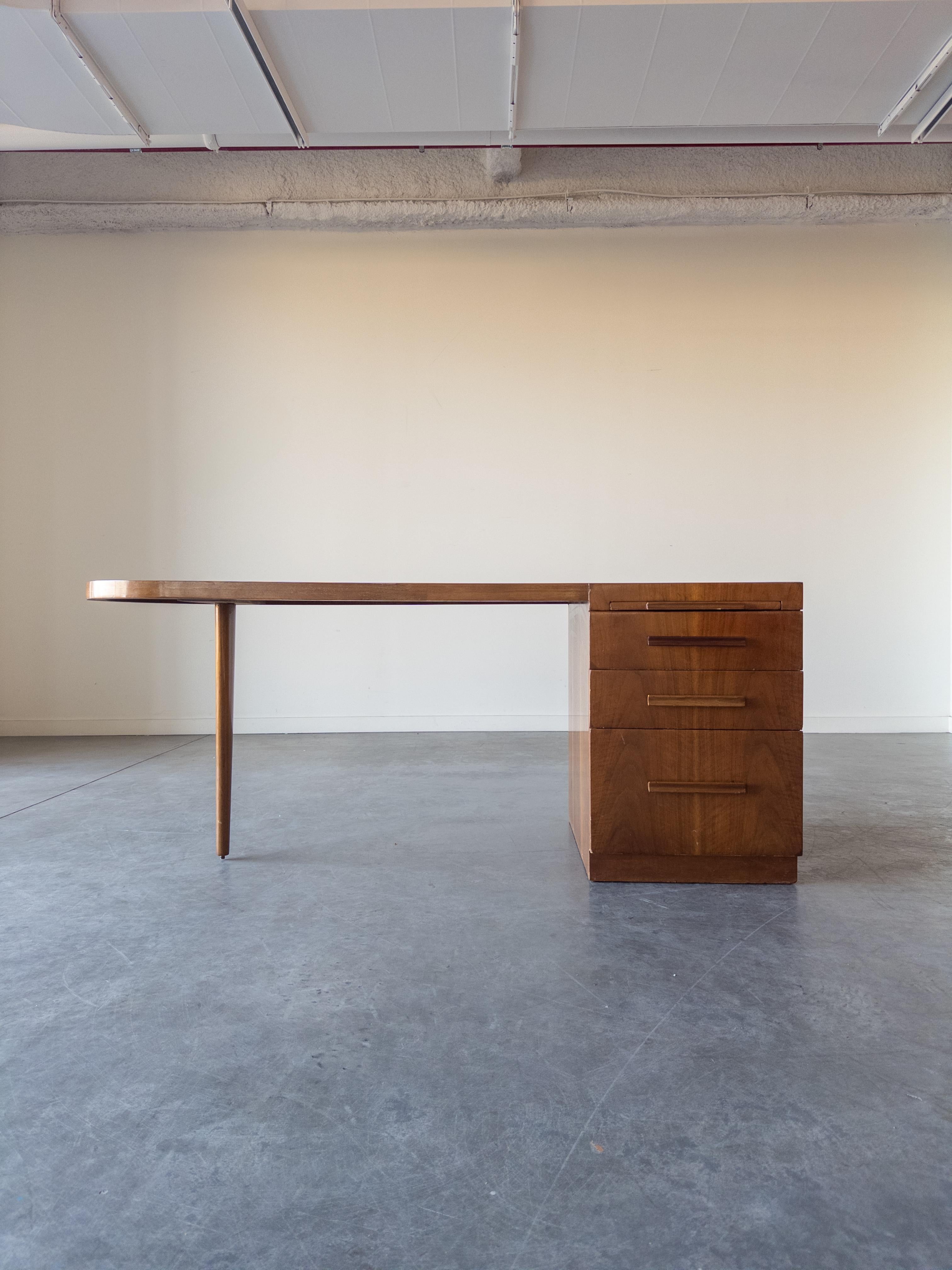 Walnut Oval Desk by T.H.Robsjohn-Gibbings for Widdicomb. American mid-century walnut desk with a top squared on the left over a set of four drawers in graduated heights with wooden bar drawer pulls, and rounded on the right, supported by a tapered