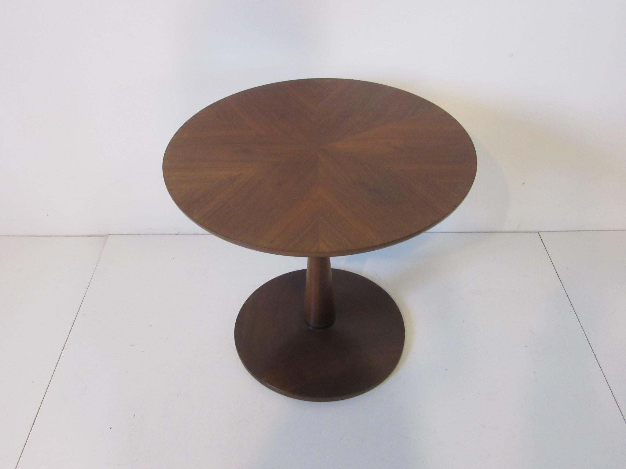 A darker rich walnut pedestal side table with bookmatched walnut top and a black ebony band to the lower bottom for detail and a round base, manufactured by the Drexel Furniture company for their declaration collection.