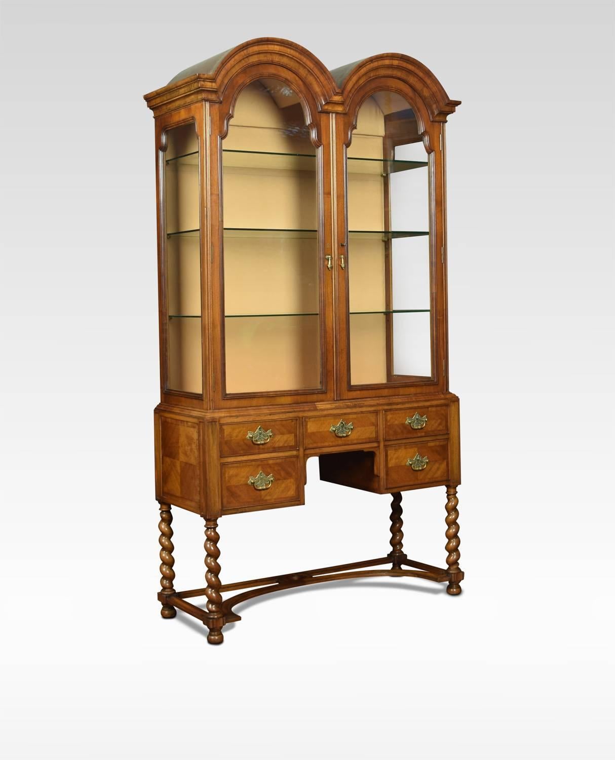 Walnut Queen Ann style display cabinet of generous proportions, the dome top above two large glazed doors opening to reveal upholstered interior with three adjustable glazed shelves. The base section with five freeze draws with tooled brass handles