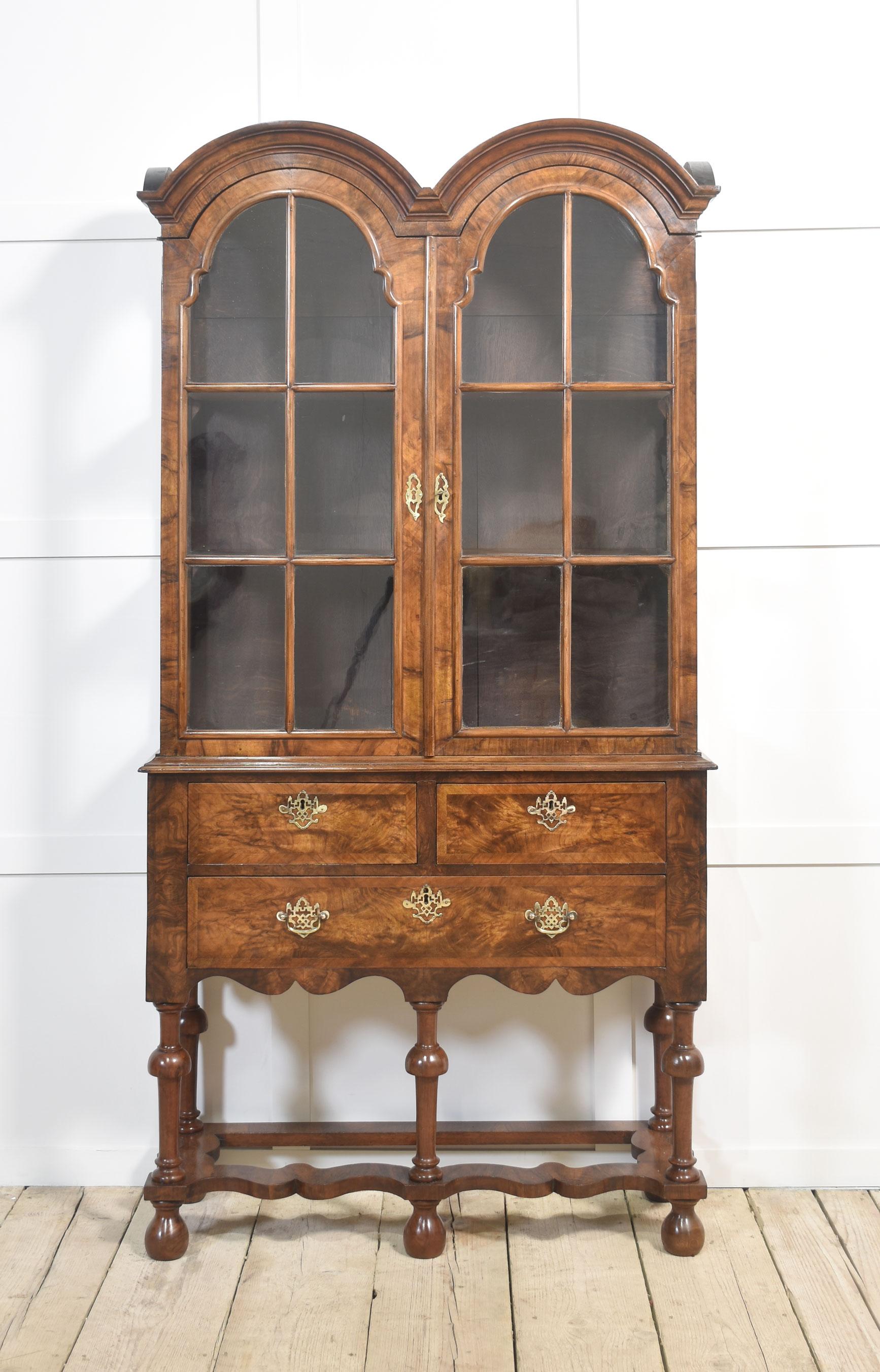 Walnut Queen Ann style display cabinet of generous proportions, the dome top above two large glazed doors opening to reveal a shelved interior. The base section having an arrangement of drawers. All raised on turned legs united by