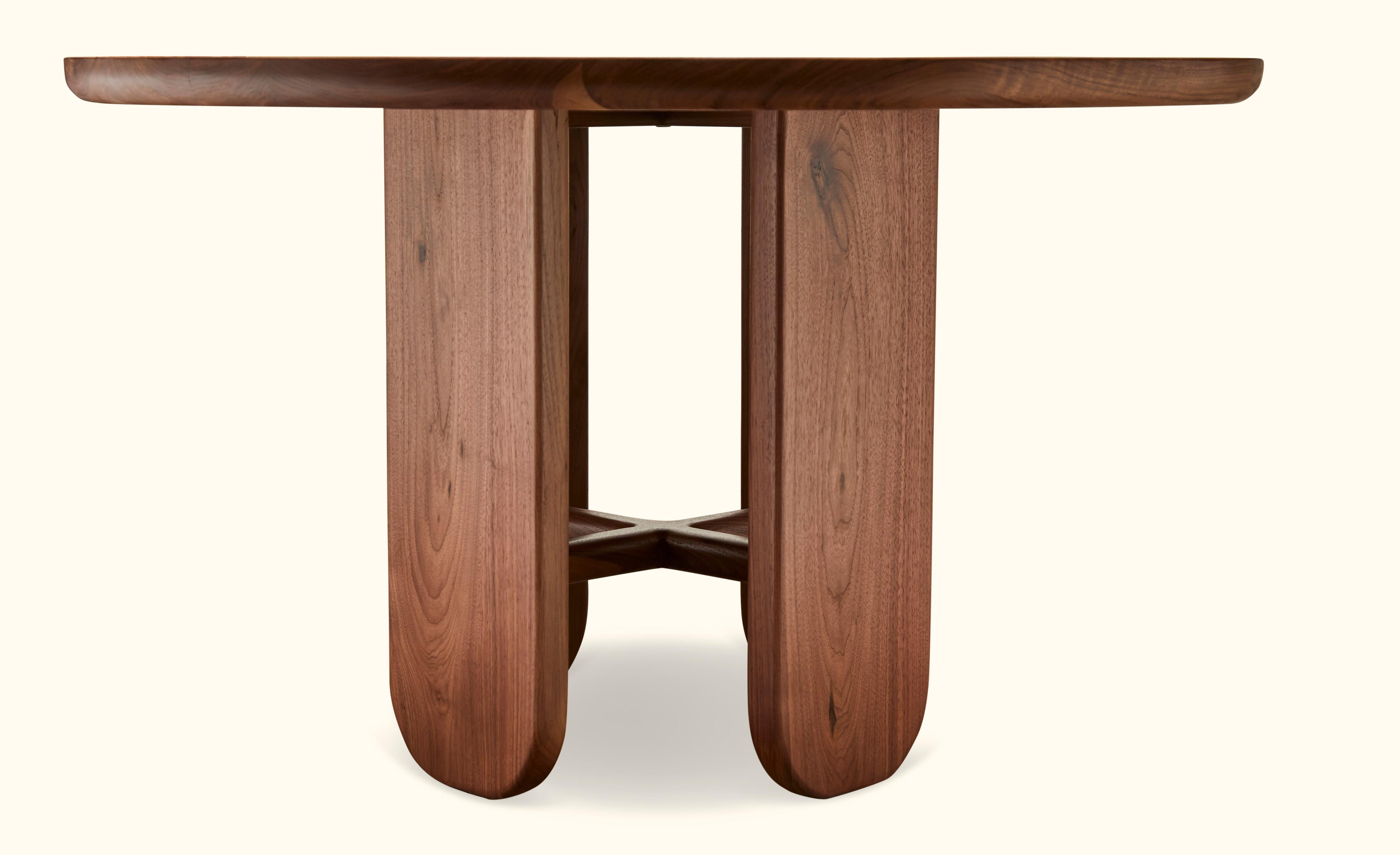 The rainier dining table is part of the collaborative collection with interior designer Brian Paquette featuring a parquet or solid wood top and four pedestal legs connected with a solid wood stretcher. Shown here in natural walnut. Available