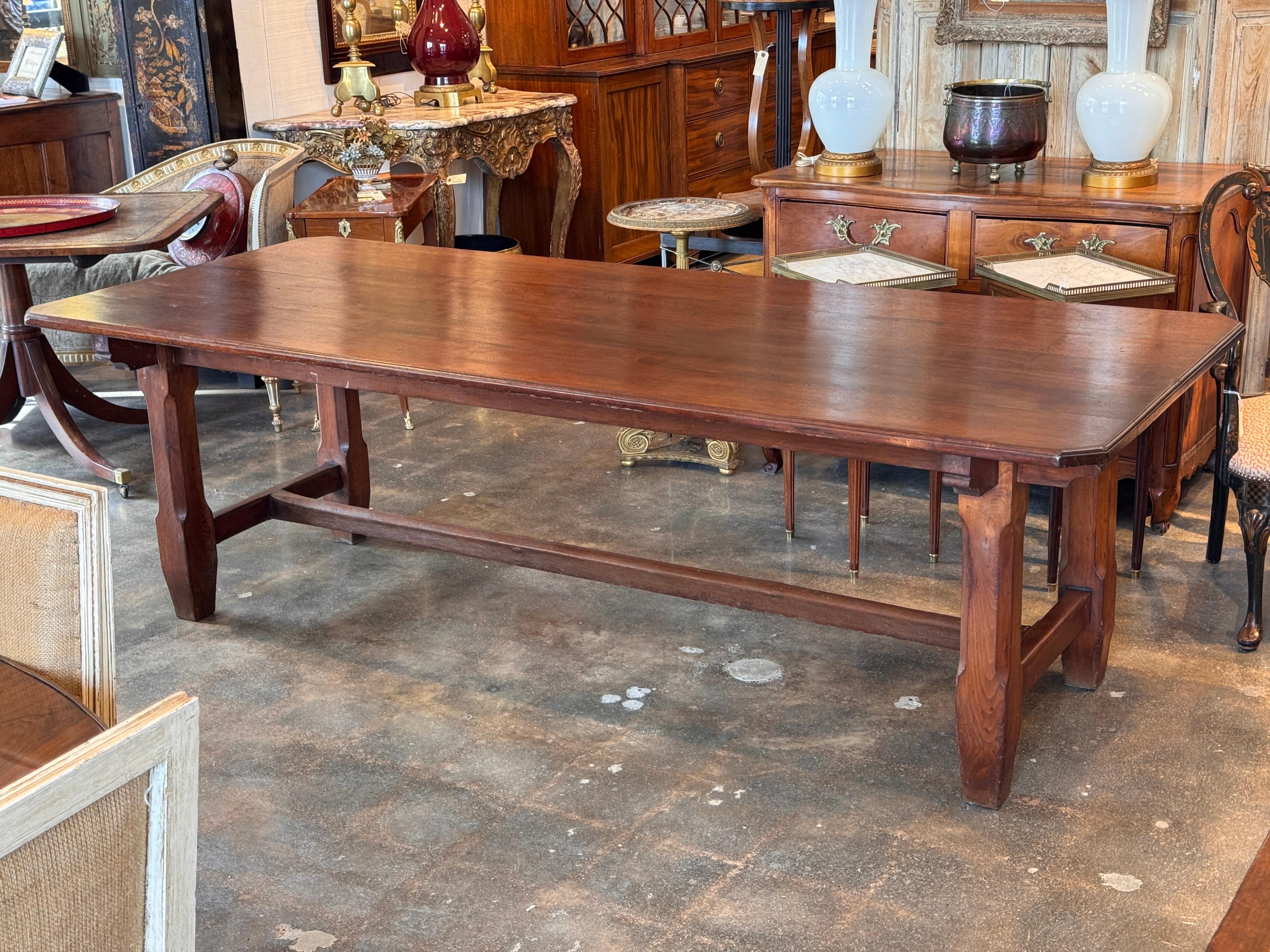 Grande table de réfectoire en noyer avec un épais plateau rectangulaire, des supports façonnés et une base à châssis. Le gros plan montre le grain chaud et la menuiserie solide des pieds et du tablier