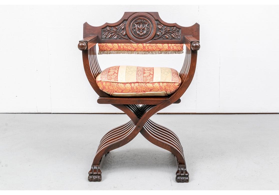 A walnut Savonarola or faldstool chair with neo-classical design, having a upholstered seat, the crest with a shield within a medallion flanked by foliate and berry motifs, carved armrests terminating with ball finials, beautiful concentric form