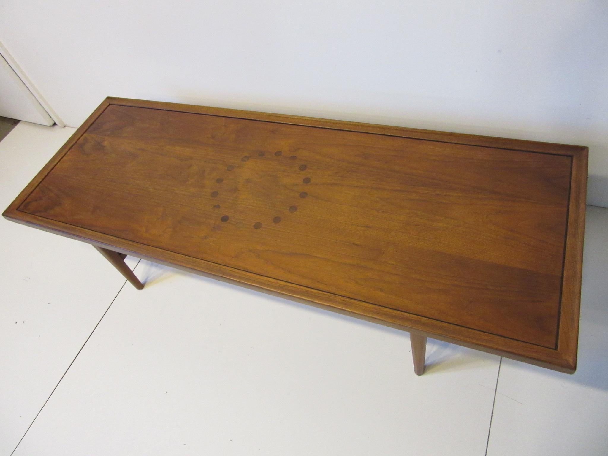 A medium toned walnut coffee table with rosewood dot design to the center of the table having inlay rosewood inset to the edge giving this well crafted table a high end Mid Century feel . Manufactured by the Drexel Furniture company for their