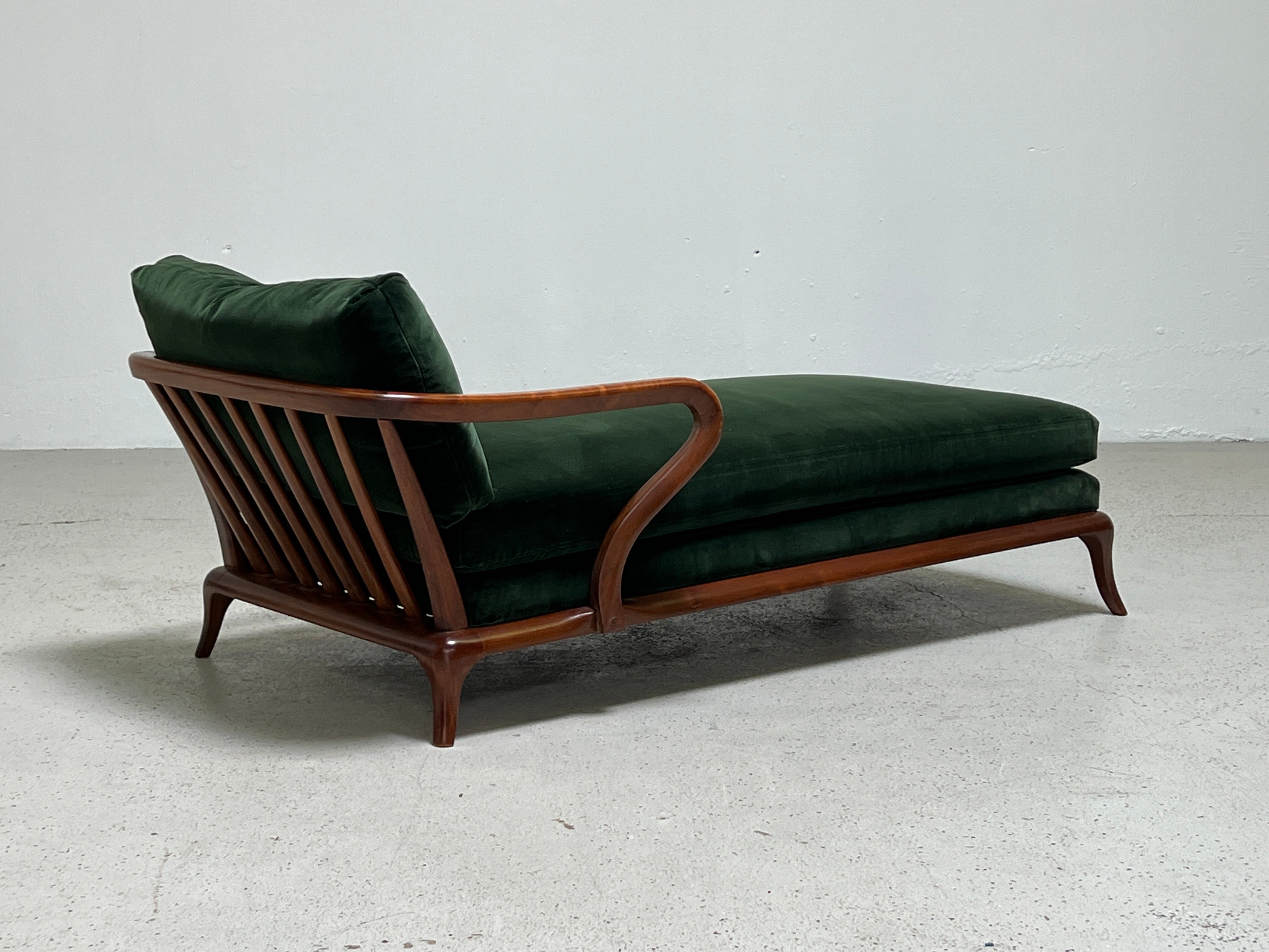 A sculptural walnut chaise lounge upholstered in green velvet.