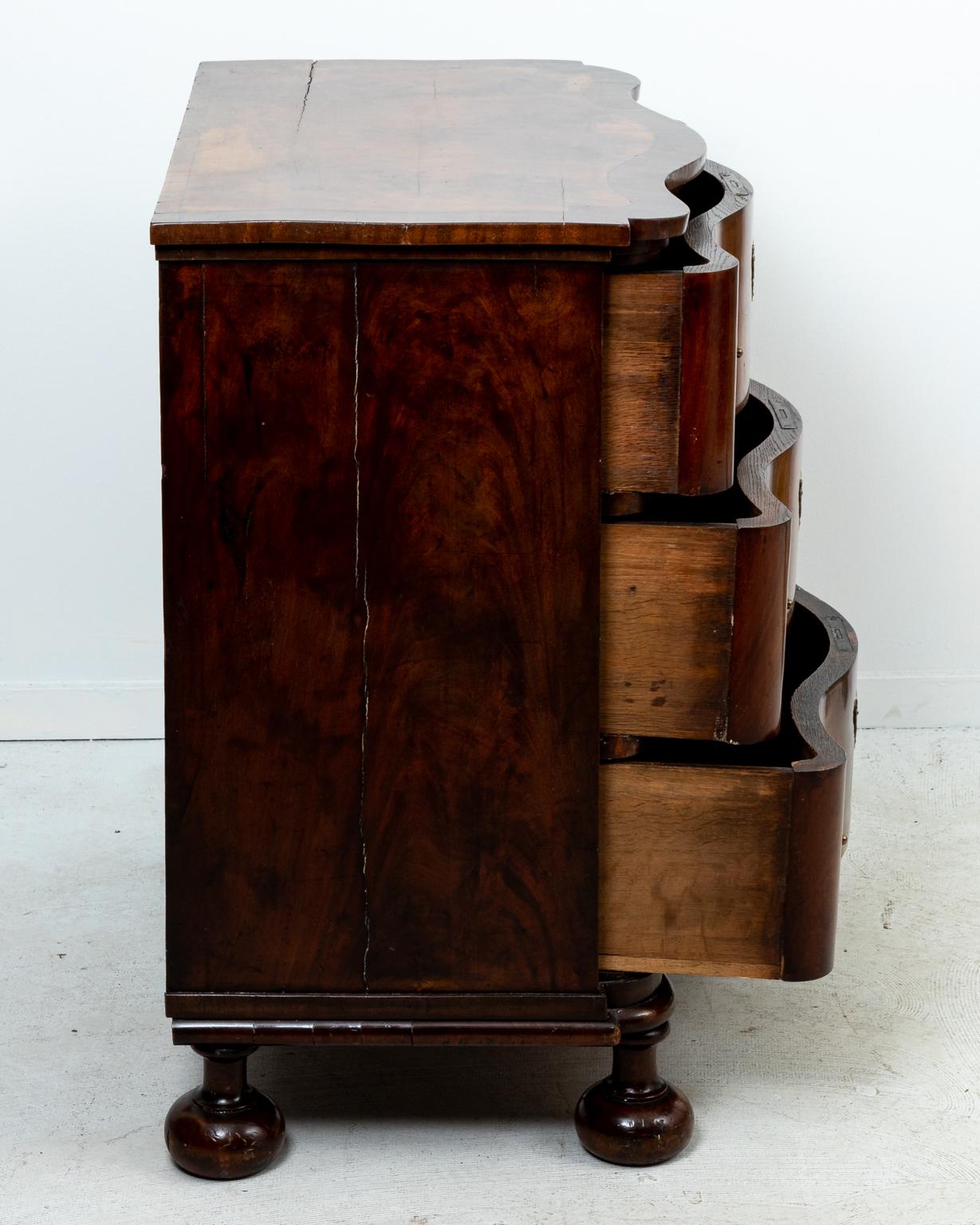 Walnut serpentine three drawer chest with metal bat's wing escutcheon. The piece also features bun turned feet. Please note of wear consistent with age including finish loss and wood loss.