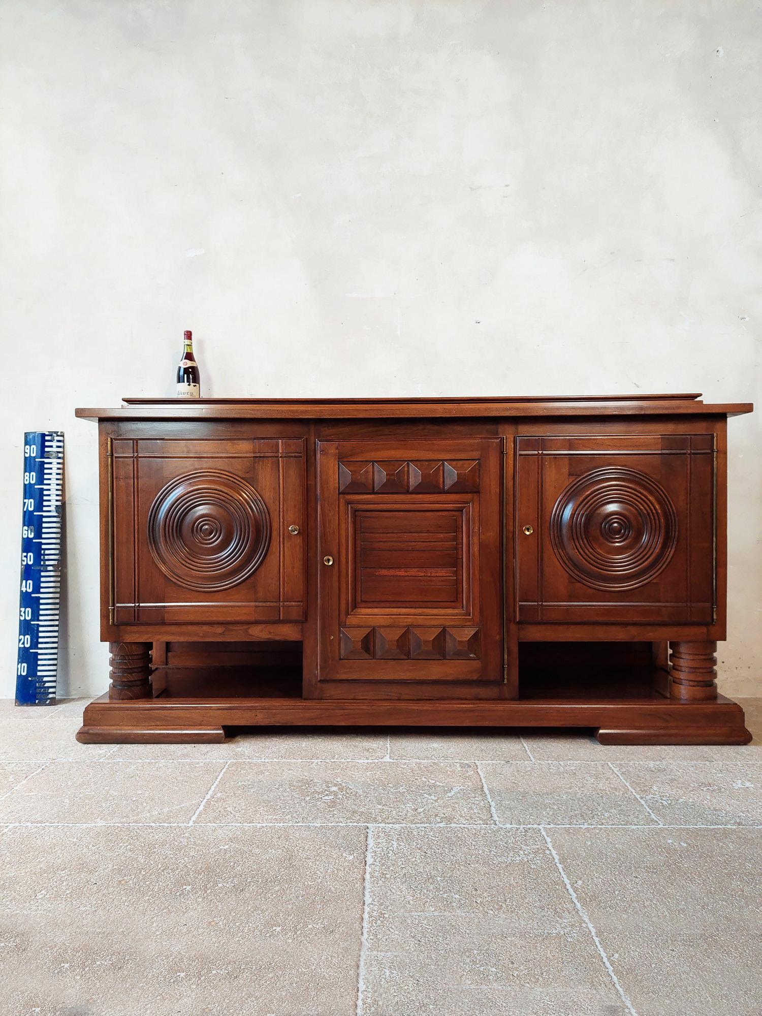 Brown sideboard by Charles Dudouyt in walnut with a polished finish, 1940s. The two outer doors with round panels and the middle door with geometrical shapes behind which are two drawers. The solid wooden frame gives this beautiful brutalist a