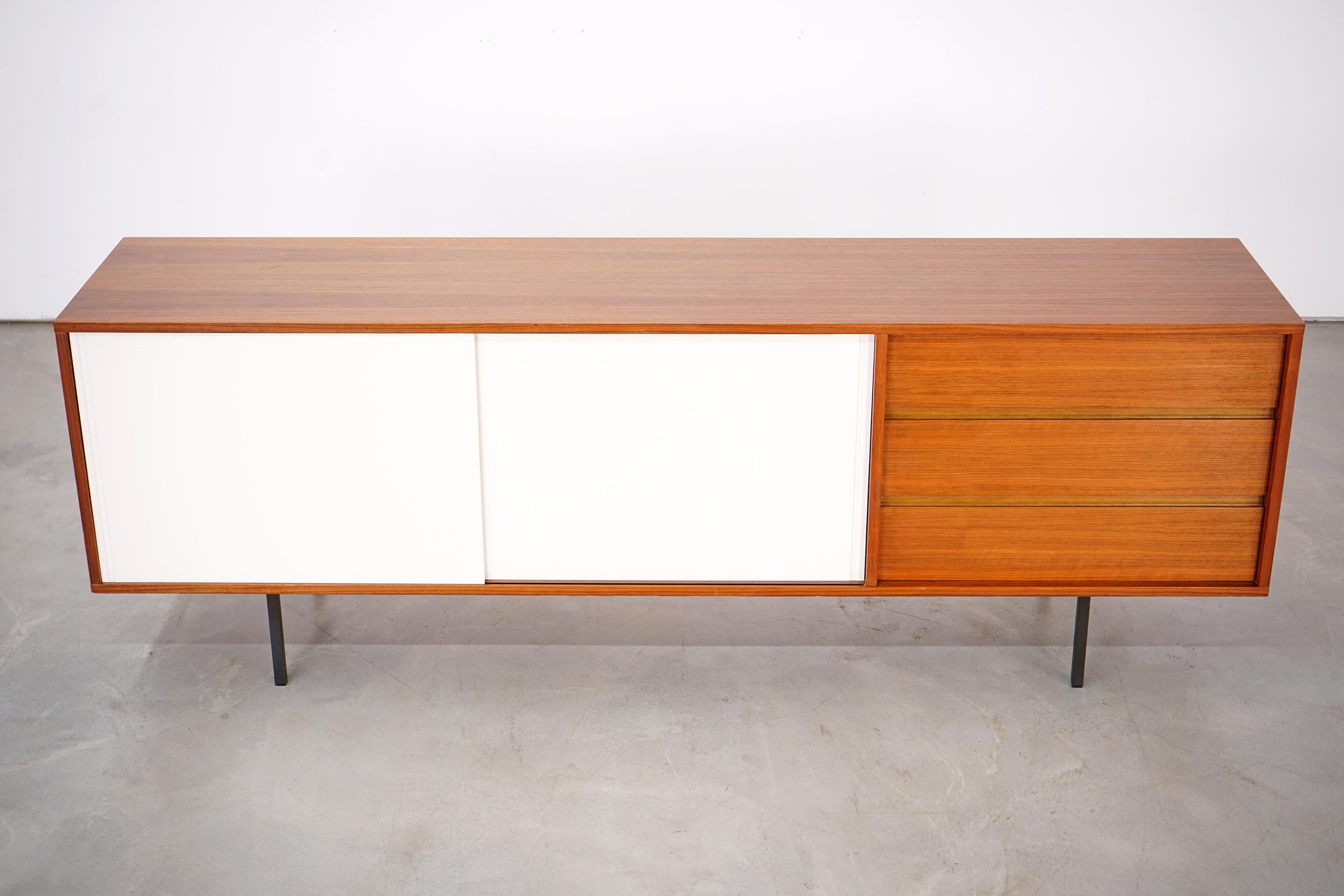 Helmut Magg designed this sideboard in the 1960s. The manufacturer Deutsche Werkstätten made the piece out of nutwood. It rests on a steel frame. The doors of the sideboard are painted white. Hidden behind these doors are two shelves. The piece of