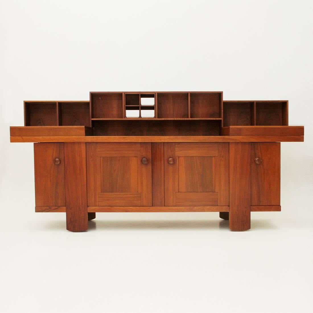 Credenza realizzata negli anni 1960 da Silvio Coppola per Bernini.
Struttura in legno impiallacciato noce.
Due scomparti centrali e due angolari con anta e mensole interne.
Piano superiore con due cassetti estraibili e contenitori