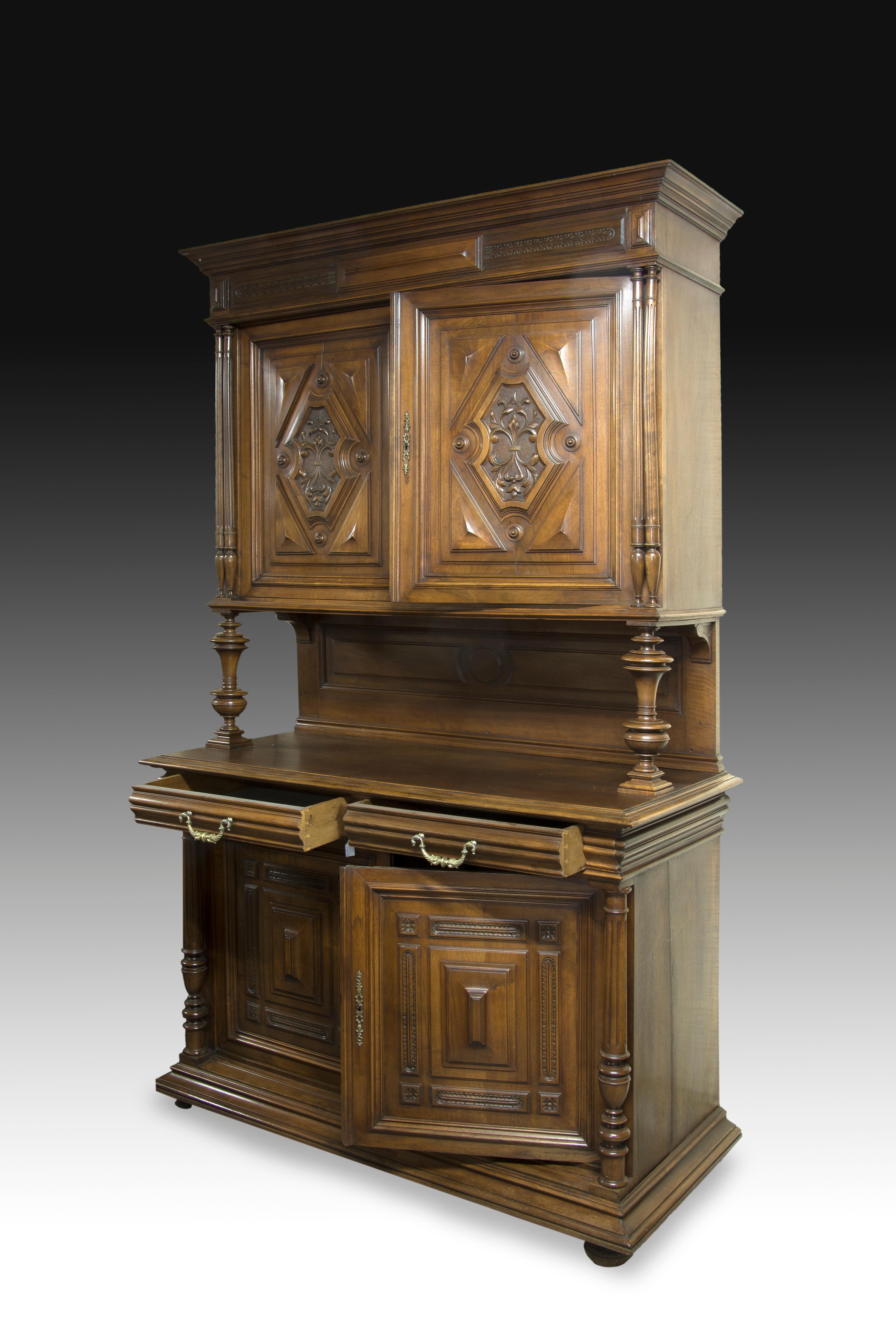 Walnut wood sideboard with two doors on the top decorated with reliefs (rhombuses, triangles panels, symmetrical vegetal composition, etc.), a space in the central area with two vase-shapped pieces and with discs on the sides , and lower area with
