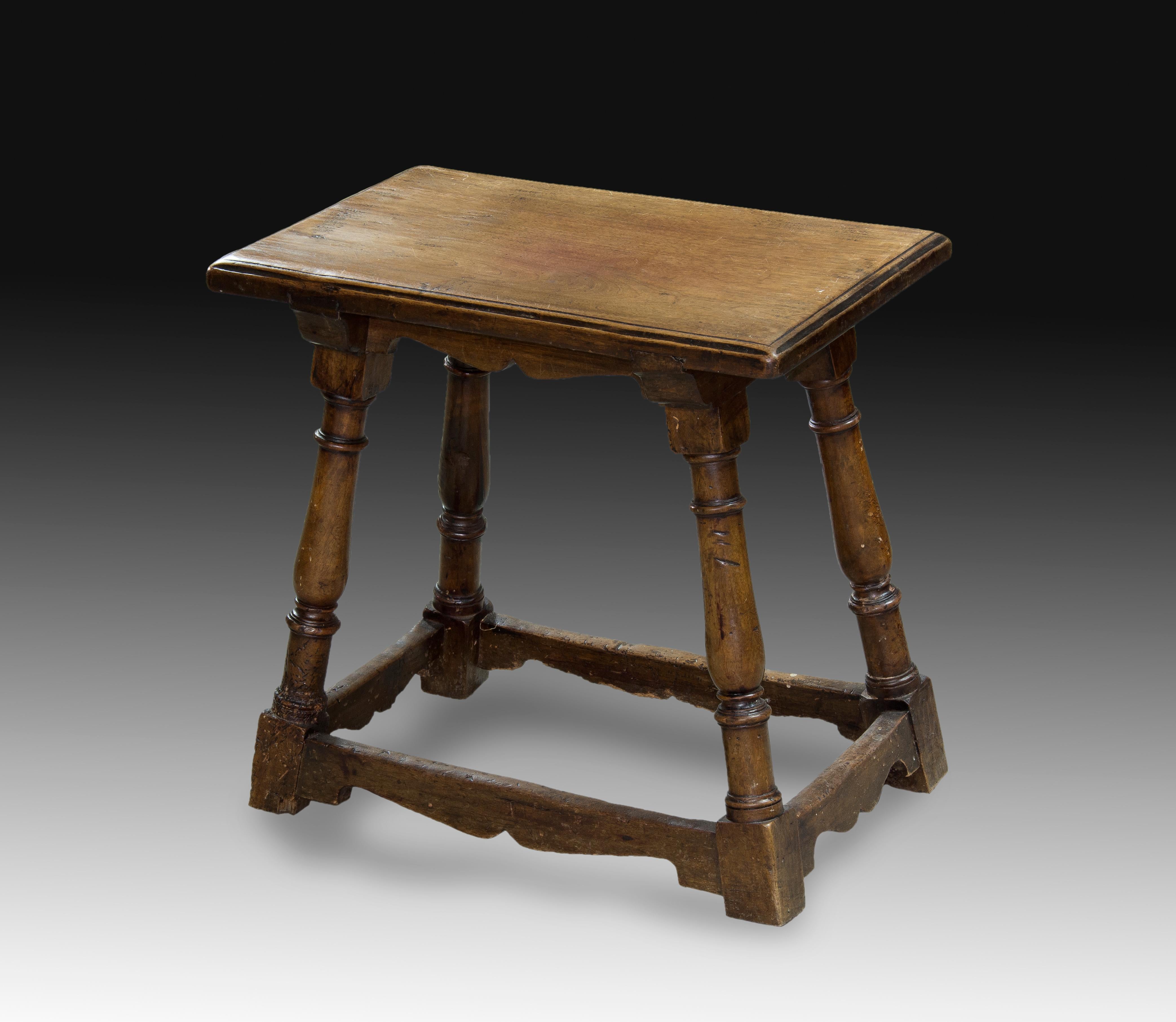 Sidewalk. Walnut wood. Century XVIII. 
Rectangular board stool with smooth molding on the edge and turned legs in the shape of balusters, which are secured in the lower area by trimmed profile chambranes in the lower part. It presents classicist