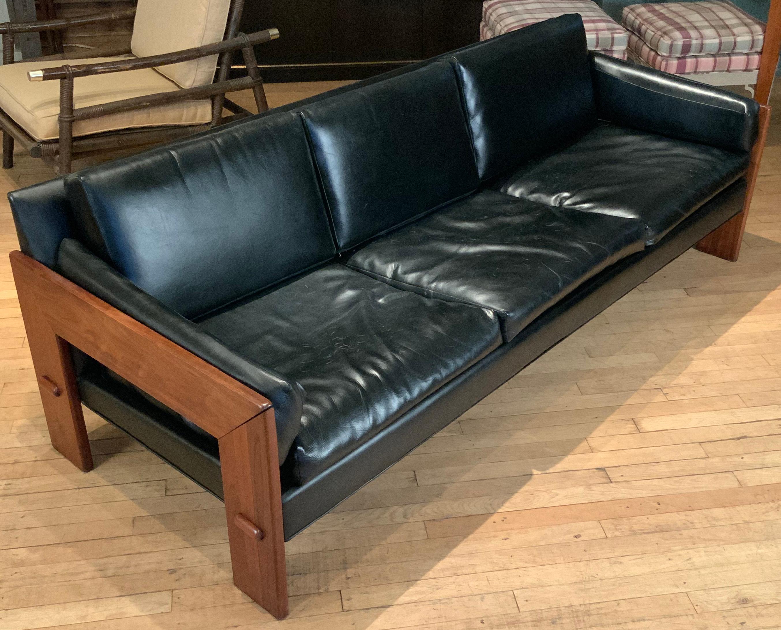 A Classic modern 1960s three-seat sofa with a solid walnut frame, with inverted U shaped ends, and its original black vinyl upholstery.