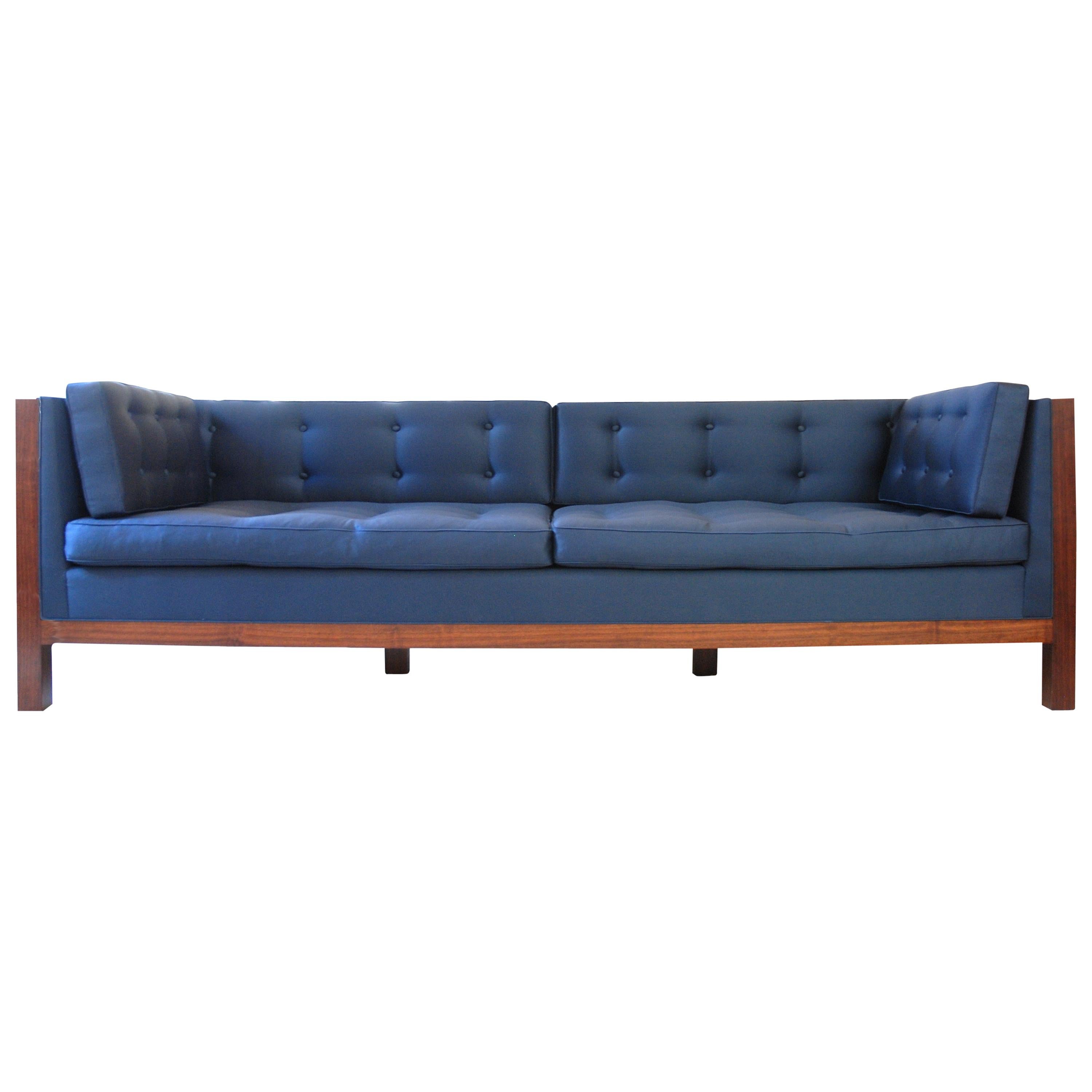 The walnut sofa has a tight upholstered frame with loose back, arm and seat cushions, which are button tufted and upholstered in a blue wool sateen textile. 

The sofa's inset panels are book-matched walnut veneer.

This item is a showroom