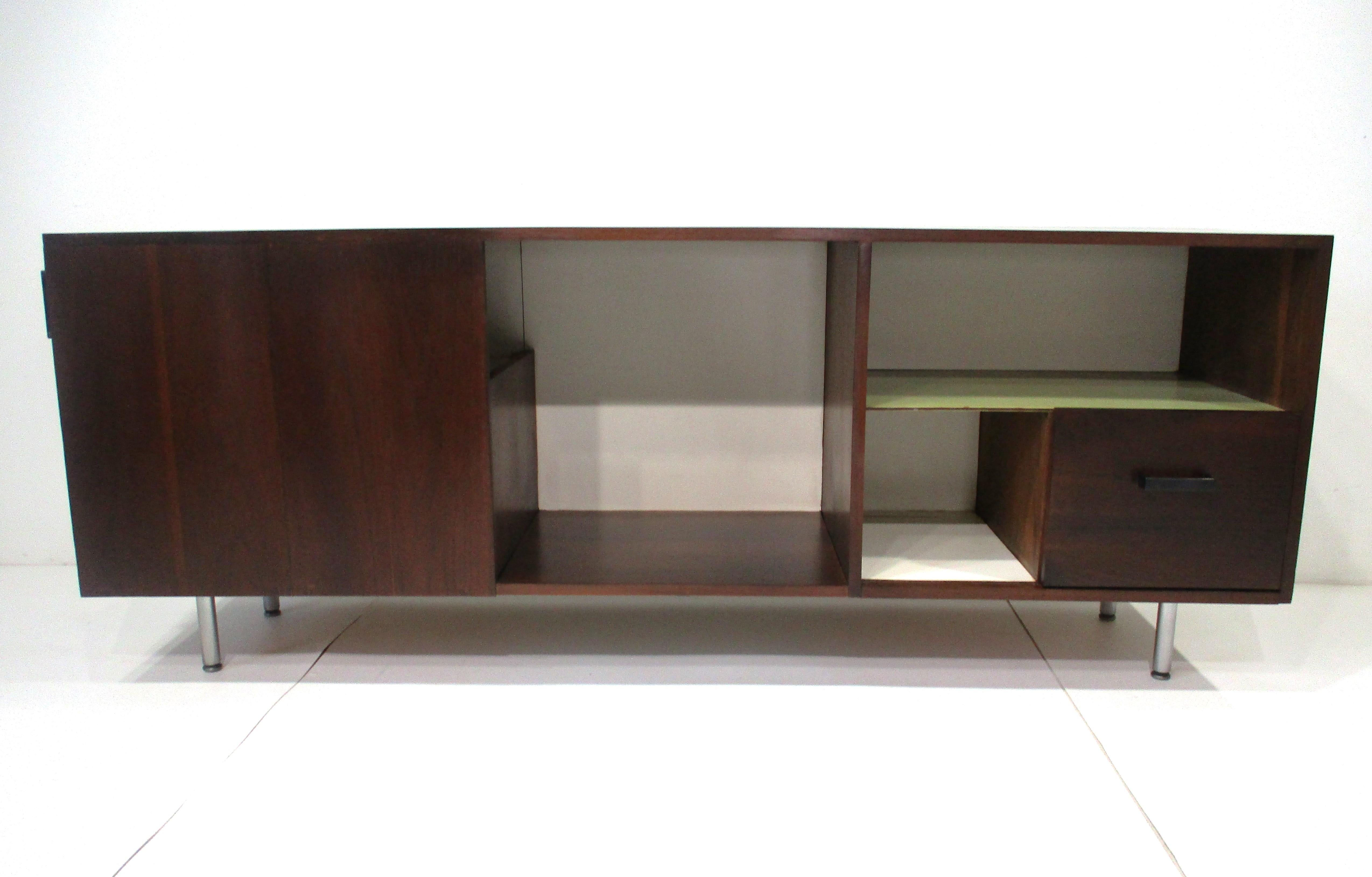 A dark walnut stereo / entertainment credenza cabinet with center storage area for records , small lower cubie and shelve for stereo equipment . There's a front drawer and side door with large storage area to one end all sitting on brushed stainless