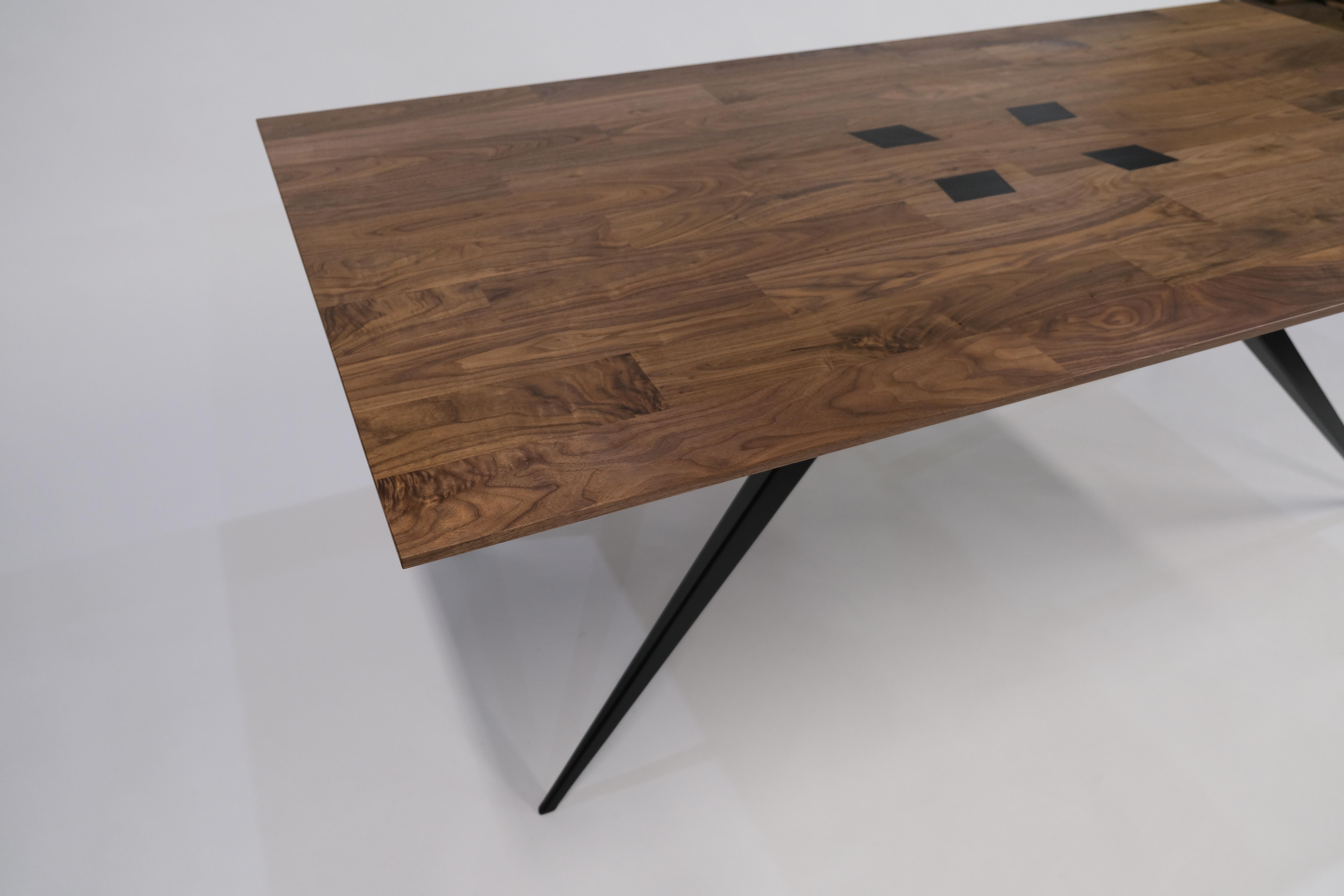 This solid walnut tabletop is beveled down to a delicate edge, and is pierced with tapered steel legs that solidly rest on the floor. 

The black finish of the steel leg tops meet the walnut hand oiled finish of the tabletop to create a flush