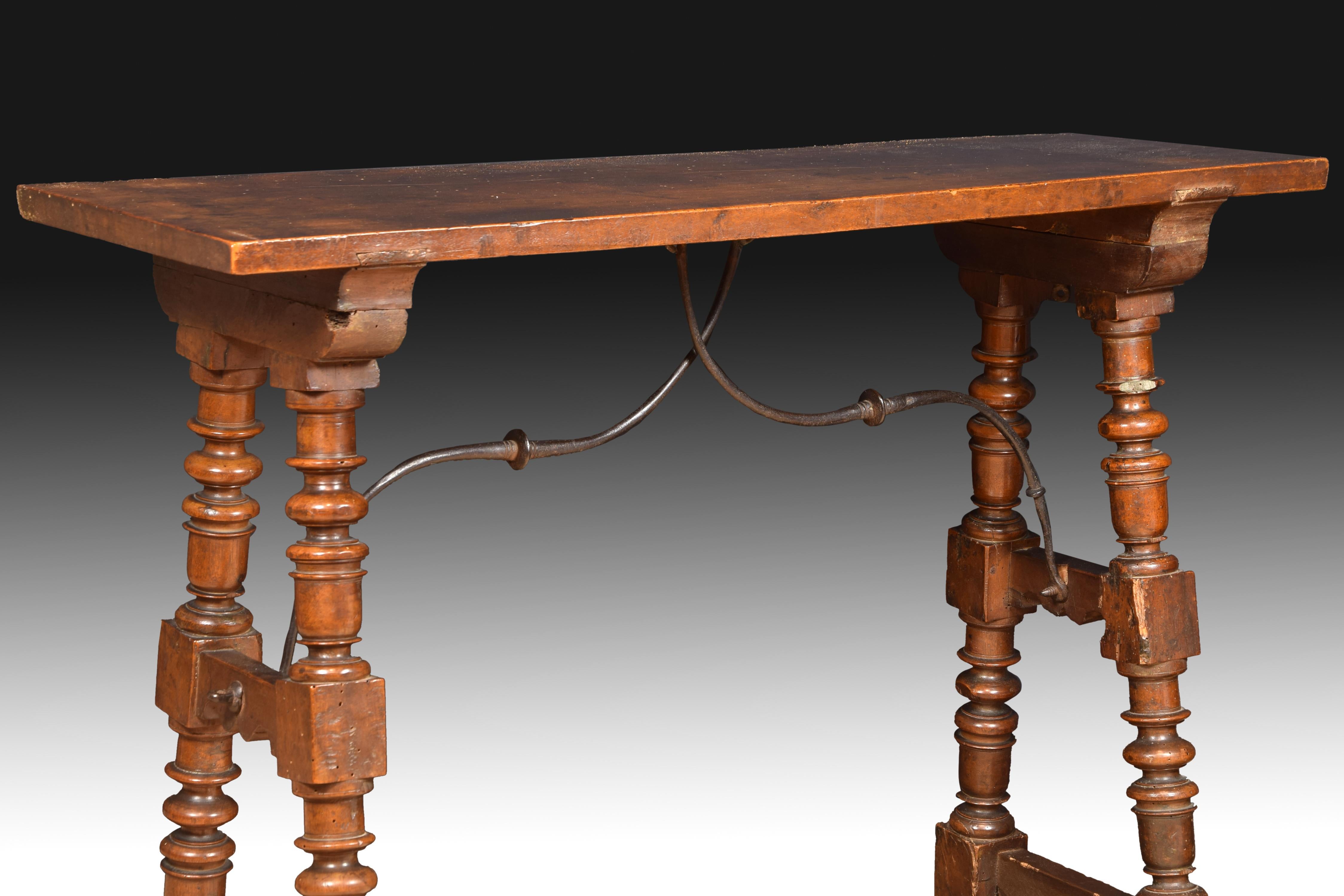 Paws turned together with double chambrana are secured to the table top with curved wrought iron fasteners. This type of furniture was made to support and display bins or desks, for utilitarian objects that, however, were often decorated moderately