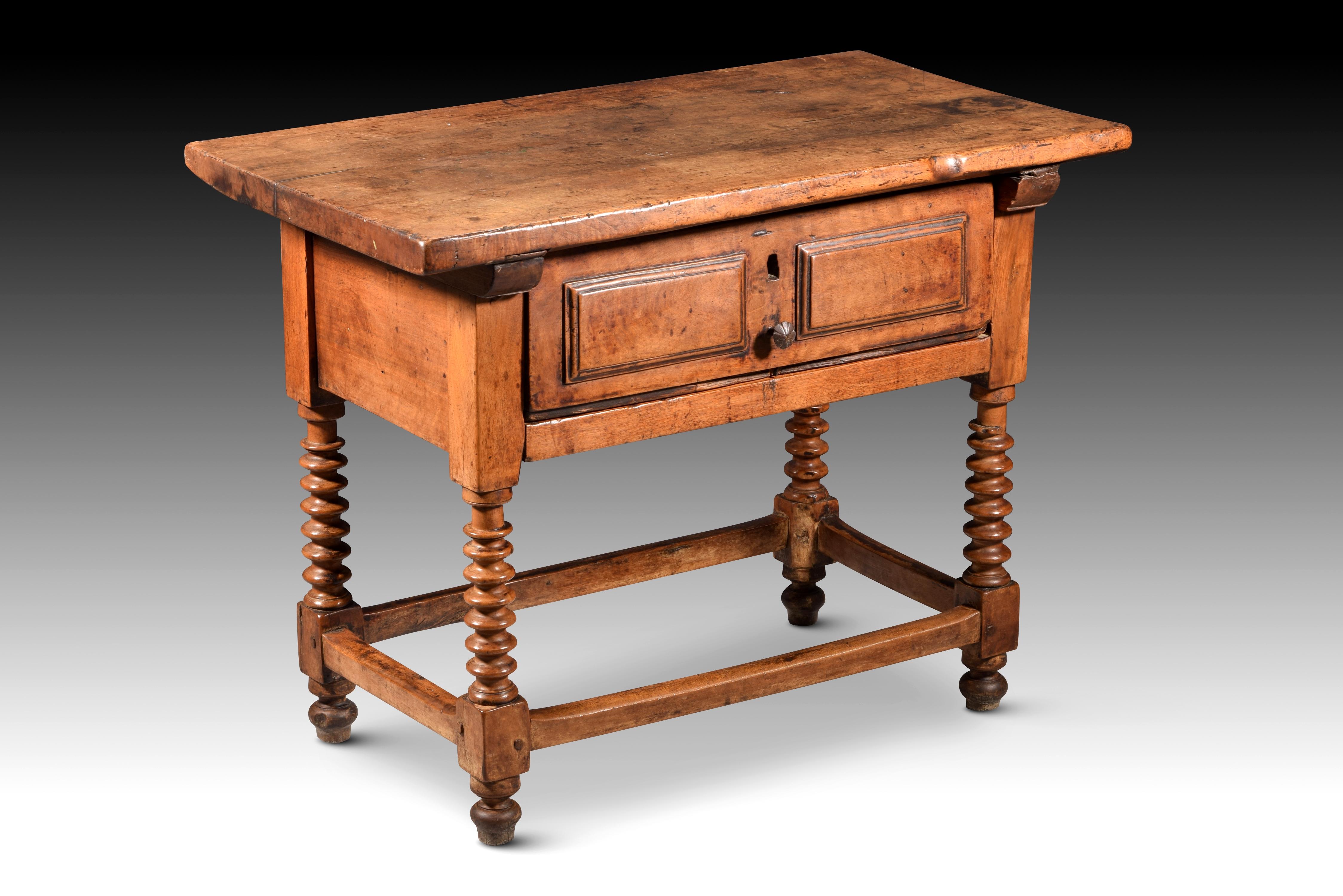 Tisch mit linsenförmigem Bein. Walnussholz. Guadalajara, Spanien, 17. Jahrhundert. 
Tisch mit einer flachen rechteckigen Platte, die an der Vorderseite eine Schublade hat, die von zwei Konsolen oder glatten Leisten flankiert wird, und die aus