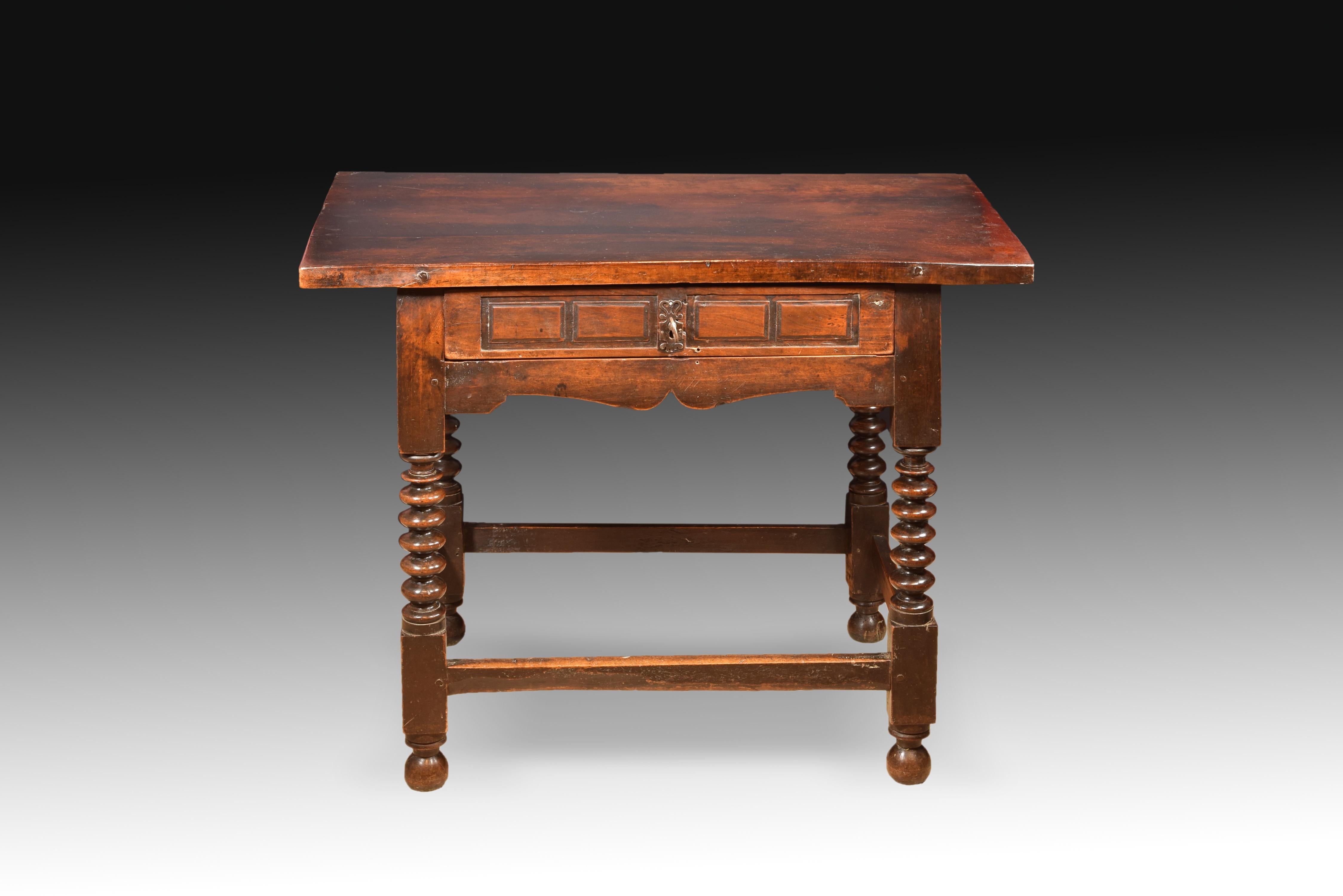 Table with rectangular upper board protruding on the sides and front drawer with rectangles carved on a lower molding curved towards the center. The four legs, located on balls, have 
