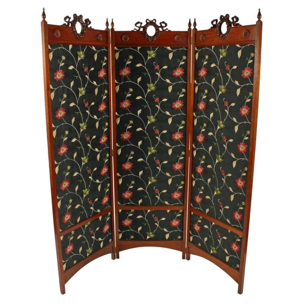 A late 19th to early 20th century walnut three fold screen with material panels.


The screen has solid walnut frames that are joined by six double action brass hinges (folding forward and back).


The top of each panel has a carved wreath