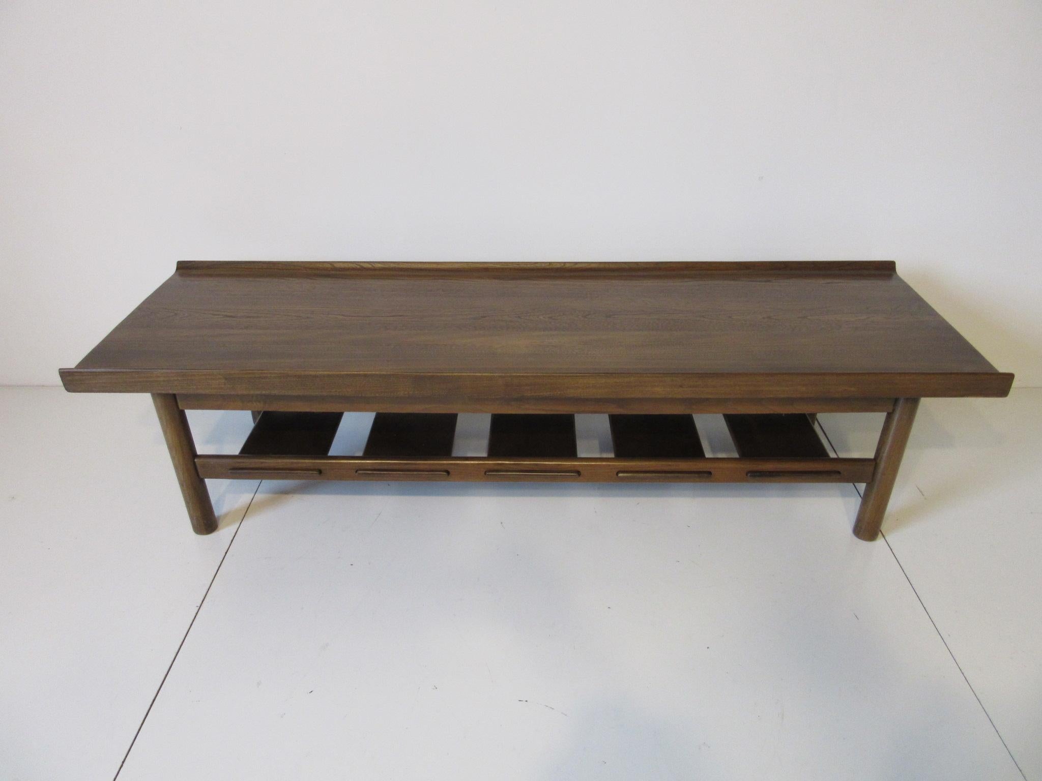 A well crafted solid plank coffee table with raised edges, rounded legs and a lower shelve with wide wood slats . Wonderful natural grain design to the top surface from the days when furniture manufactures had use of the old growth wood . This table