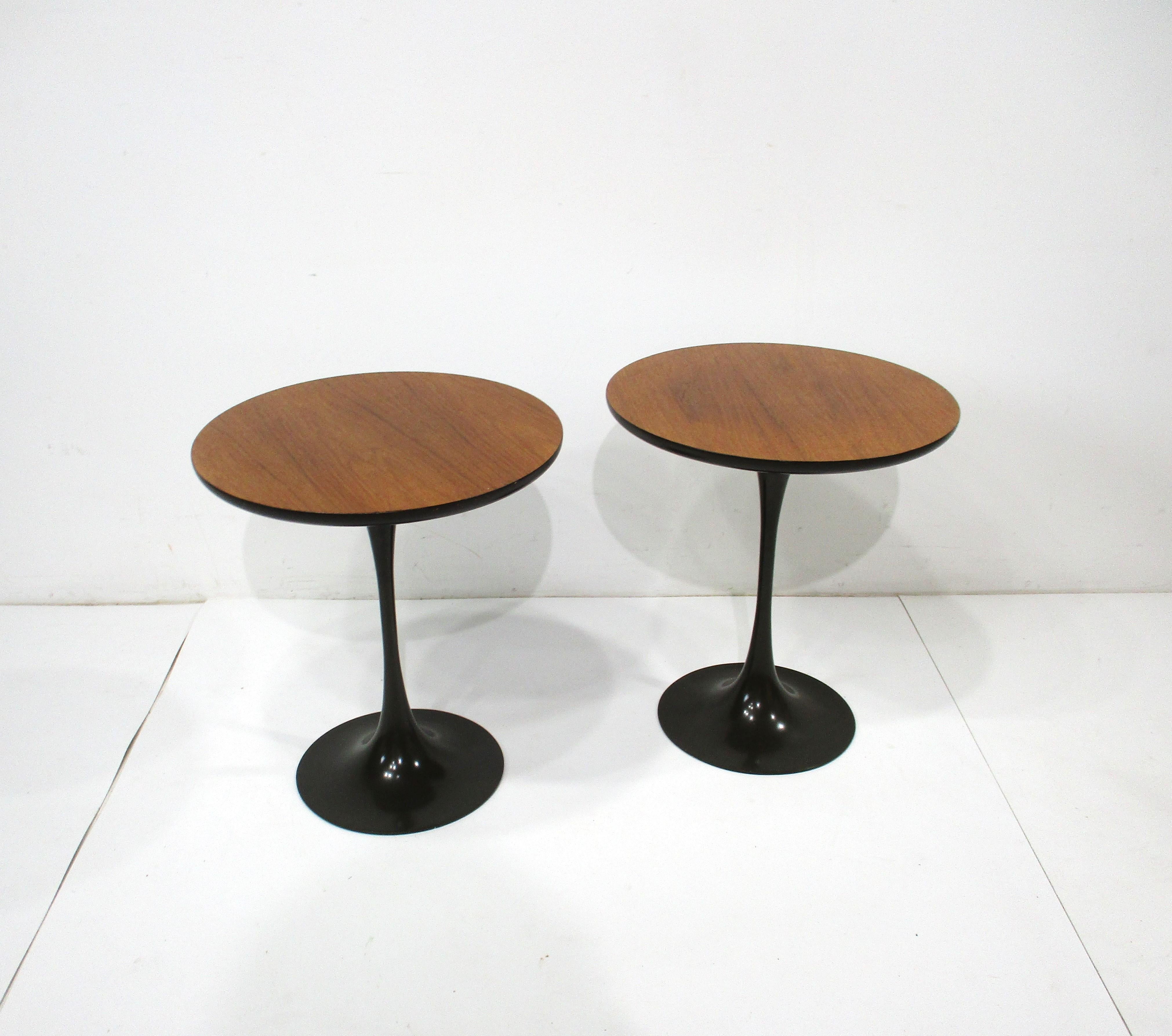 A pair of walnut topped tulip side tables with dark taupe colored steel bases designed by Maurice Burke . Rich well grained walnut and the dark bases give the pieces a sophisticated Mid Century look perfect to finish off that room . Manufactured by
