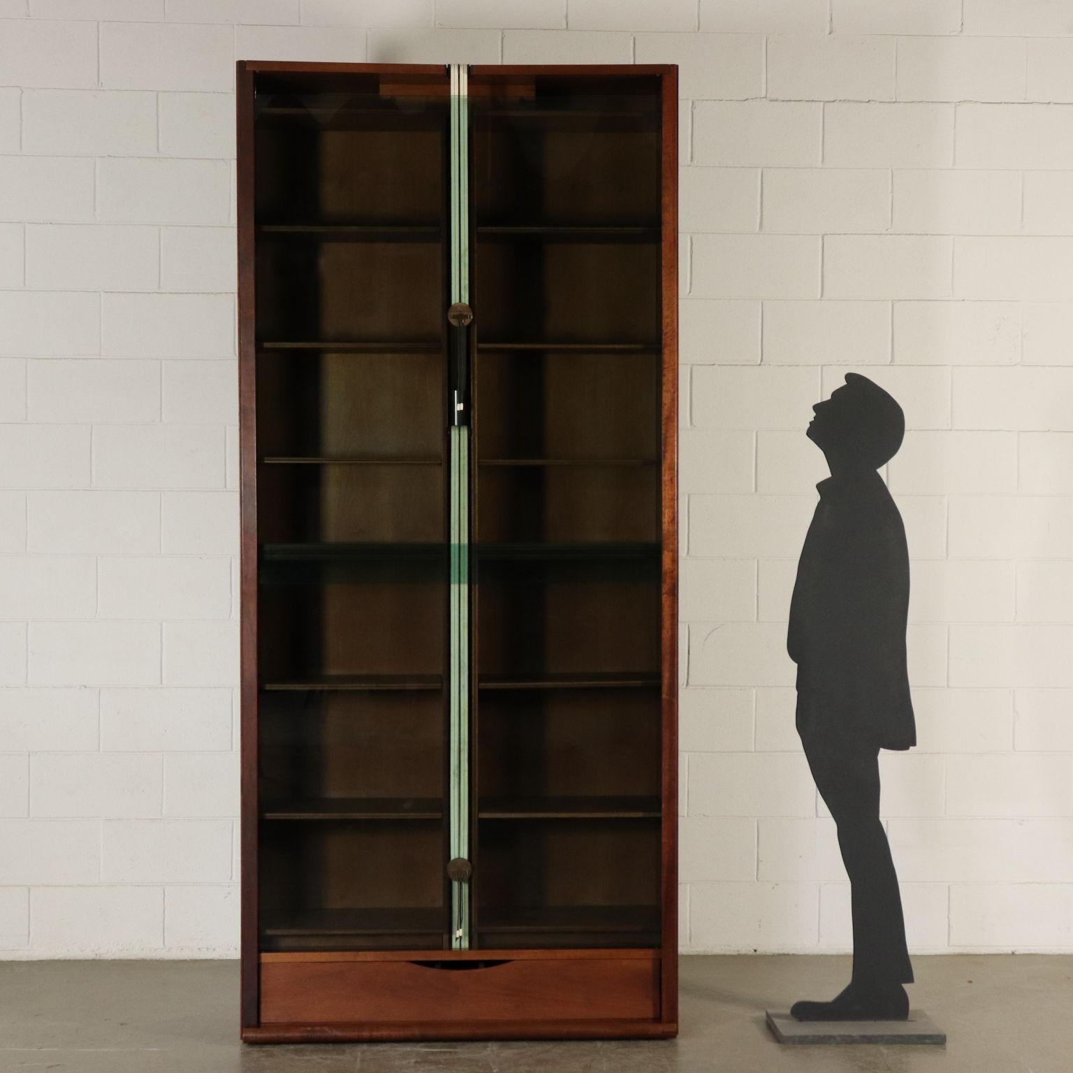 A walnut veneered bookcase with vertical sliding glass doors with counterweight. Designed by Carlo Scarpa for Bernini. Italy, 1970s-1980s.