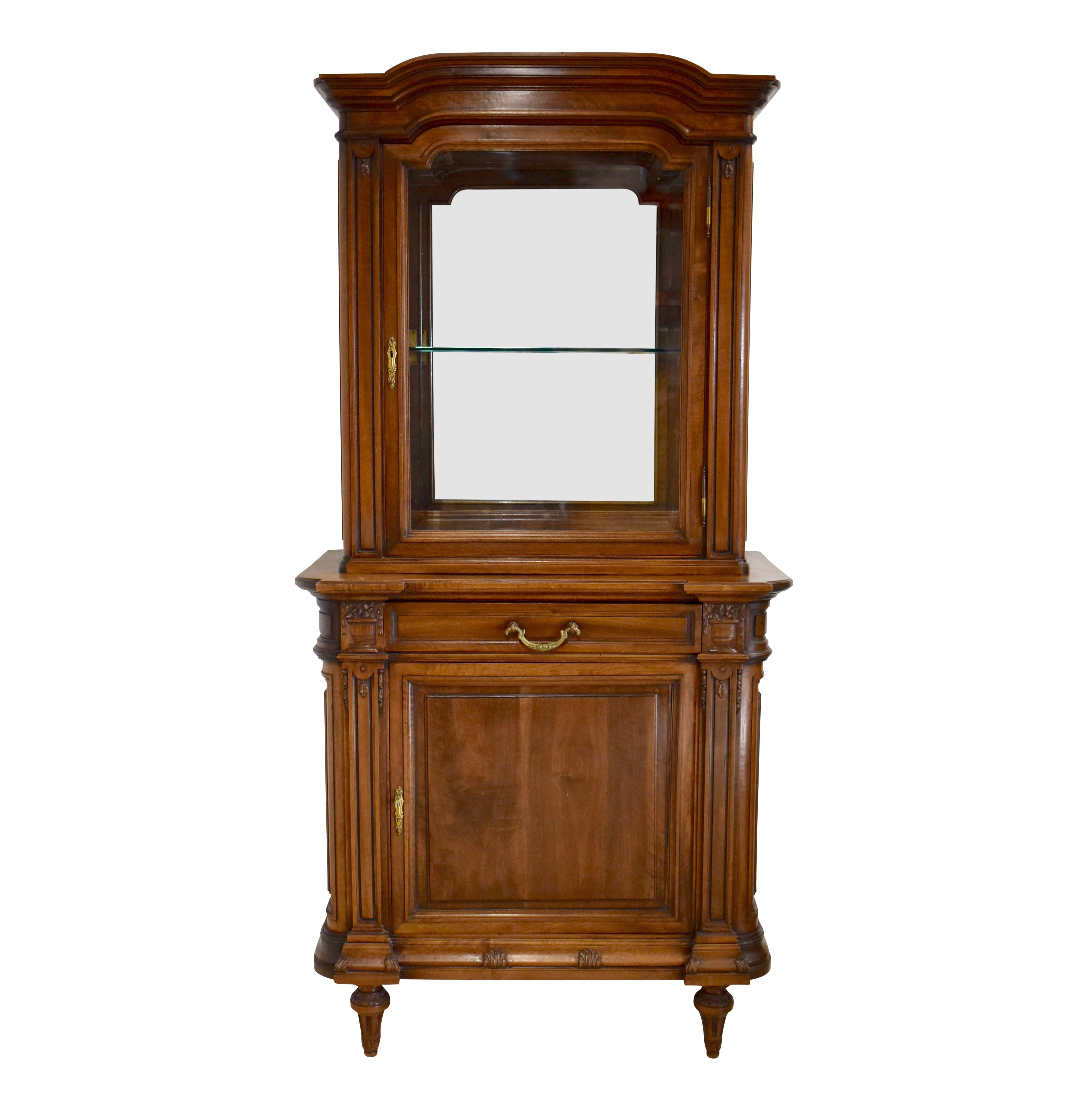 Generous storage and a delightful display case are paired in this remarkable vitrine. Crafted from beautiful walnut at the beginning of the twentieth century, the vitrine showcases a shaped bonnet, carvings of dainty flowers in planters at the