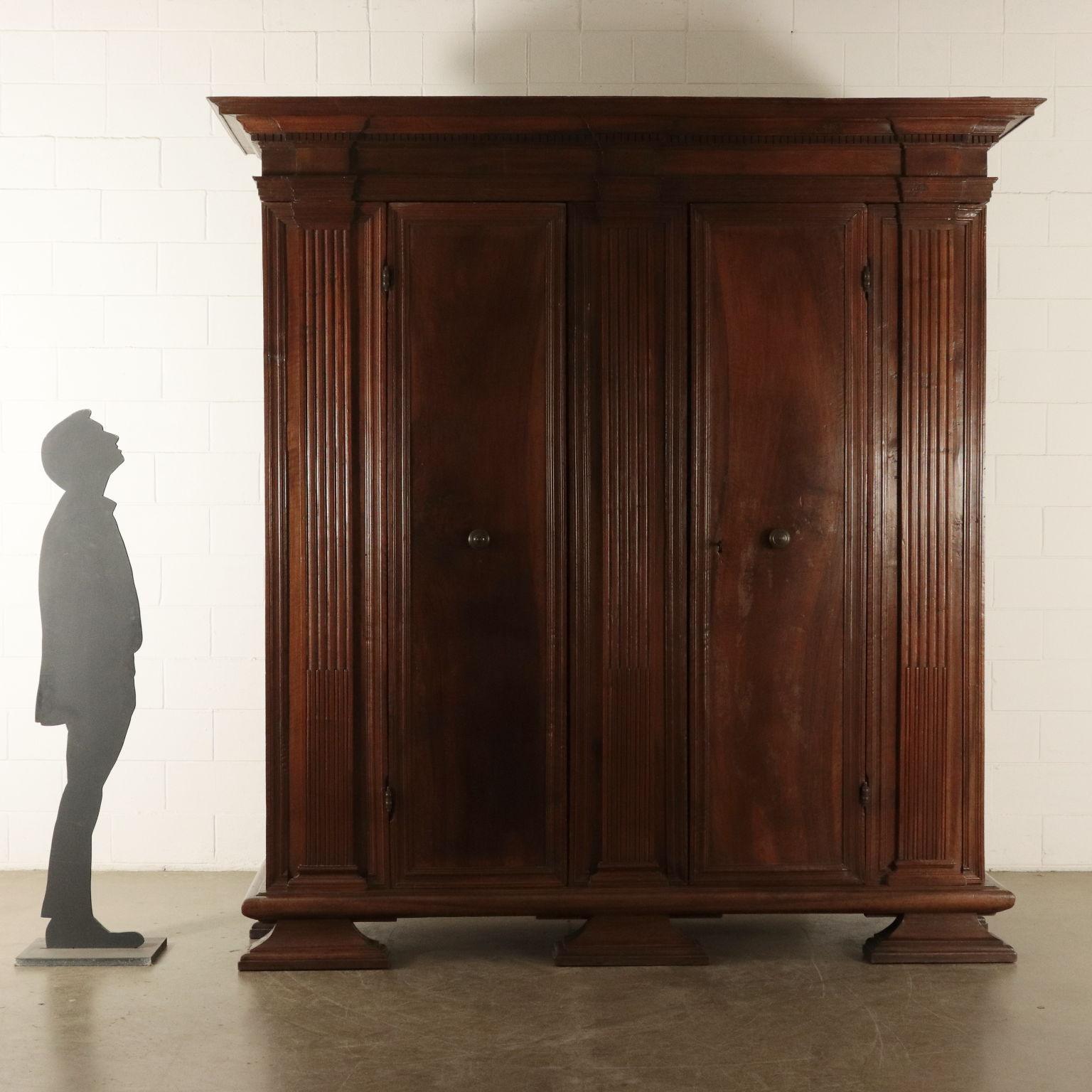 Important antique wardrobe with three big double bracket feet. It has three cabled uprights and two doors with bronze knobs, made with one framed walnut board. The upper part is decorated with several orders of frames and a notched frame.
