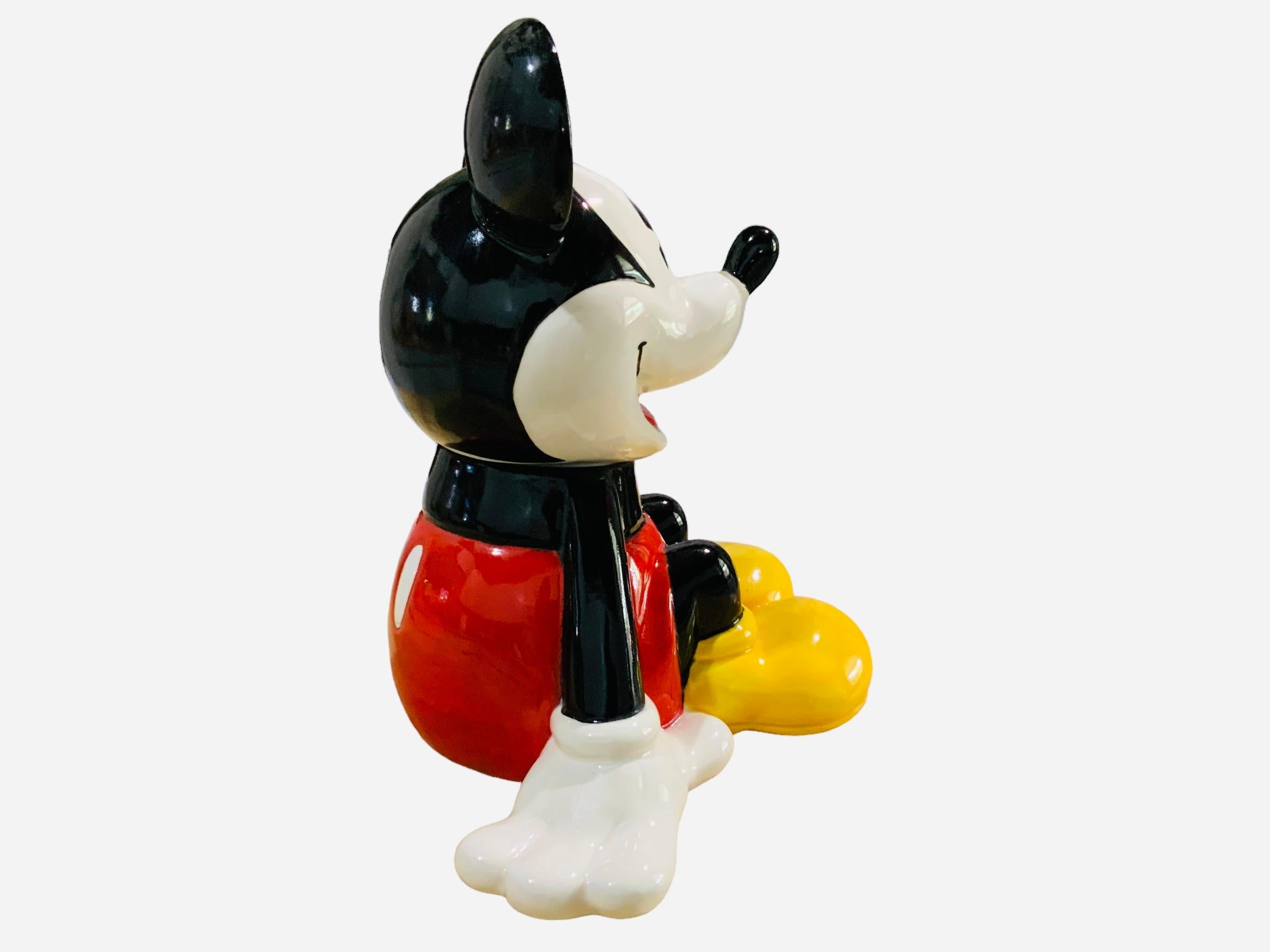 This is a Walt Disney, Mickey Mouse Cookie Jar. It depicts a hand painted glazed ceramic cookie jar shaped as a seated smiling Mickey Mouse. Below the base is hallmarked Mexico.