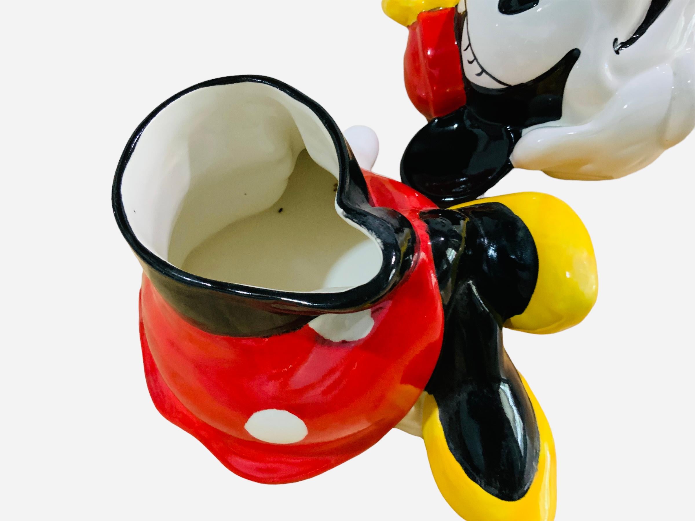 This is a Walt Disney, Minnie Mouse Cookie Jar. It depicts a hand painted glazed ceramic cookie jar shaped as a flirty seated Minnie Mouse. Below the base is hallmarked Mexico. The border of her head lid is hallmarked C, Disney.