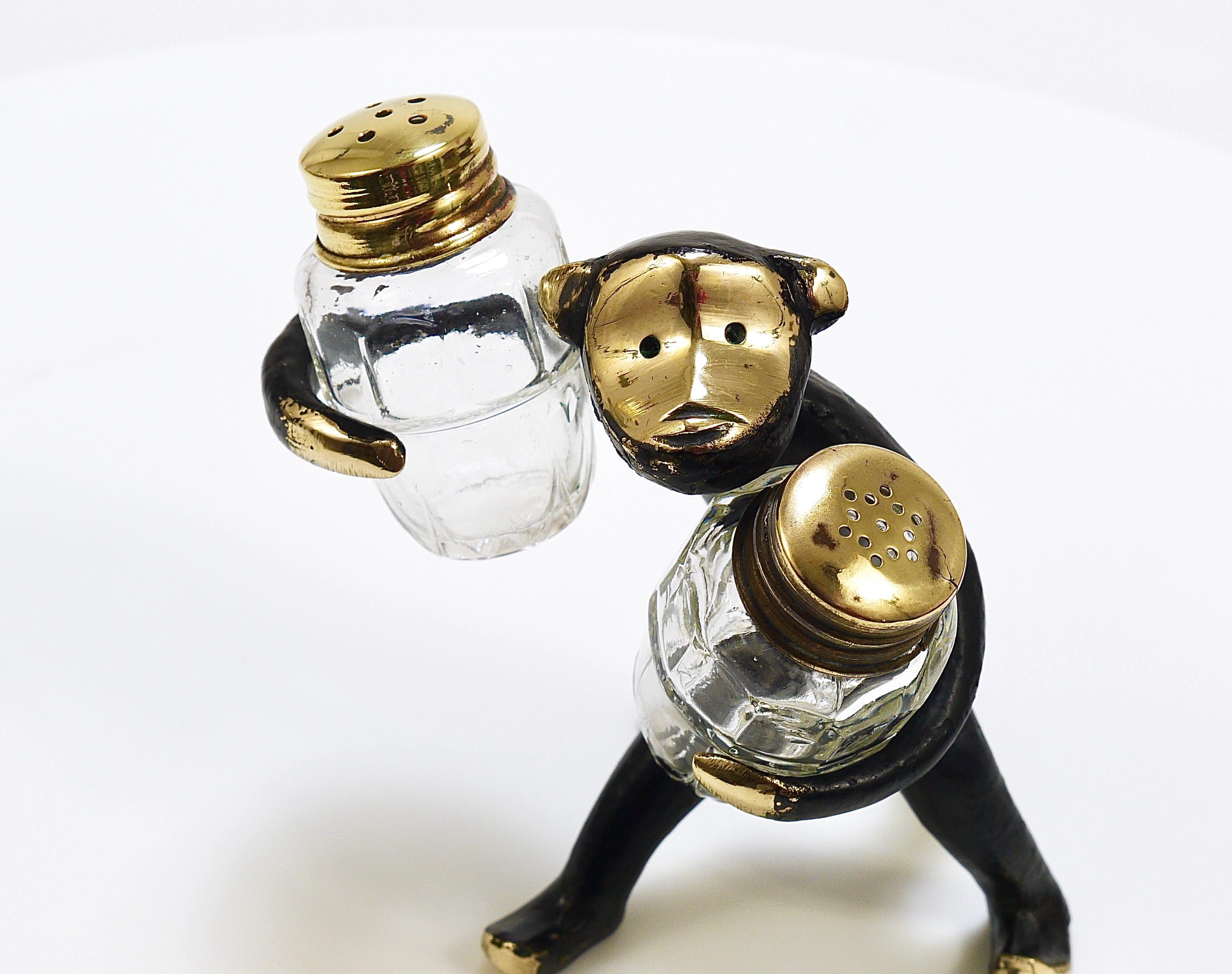 A charming Austrian midcentury shaker set from the 1950s, displaying a cute monkey holding salt and pepper shakers. A humorous design by Walter Bosse, manufactured by Hertha Baller in Vienna, Austria. Made of blackened brass, in good condition with