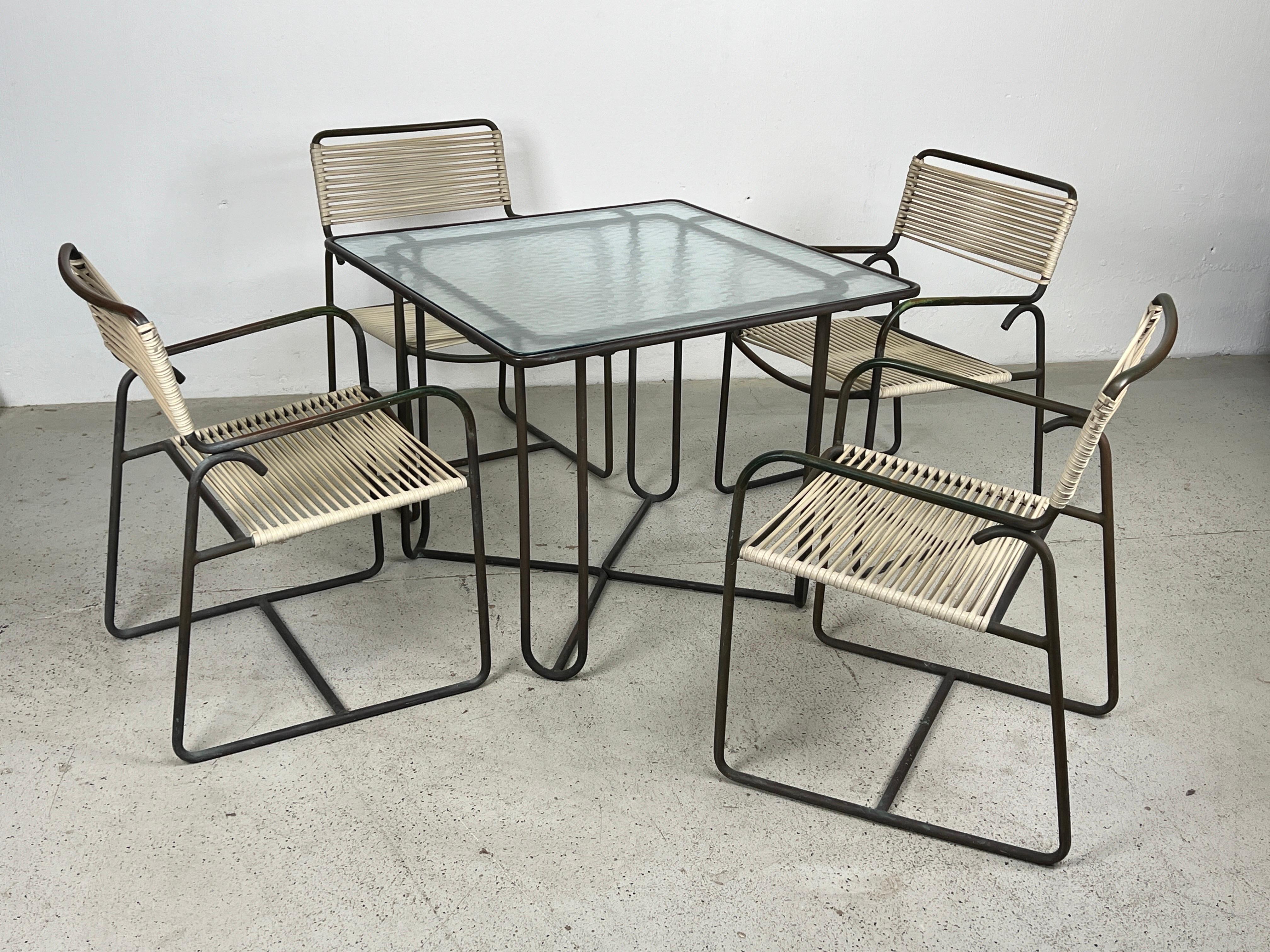 A beautifully patinated bronze patio set by Walter Lamb. The set consists of two dining tables and four arm chairs that can be used together or separate. The set is all original and in wonderful condition. The original vinyl cording is in tact and