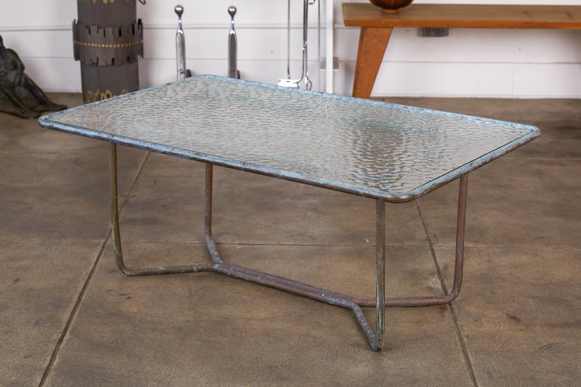 A patio coffee table in patinated bronze designed by Walter Lamb and produced by Brown Jordan. The table has a rectangular shape with rounded corners, supported by bunt tubular in matching bronze. The legs are joined by diagonal stretchers and a