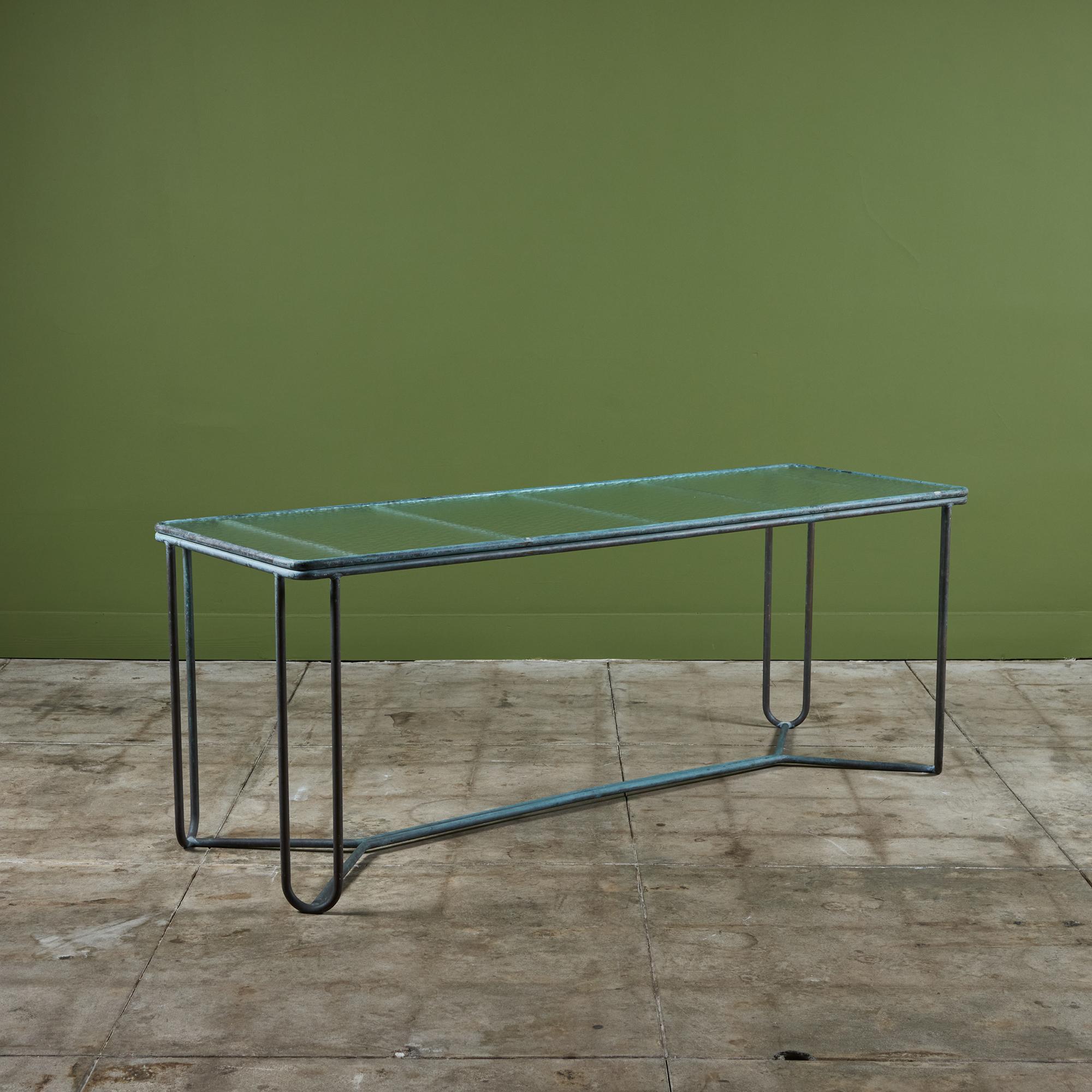 A patio console table in patinated bronze designed by Walter Lamb and produced by Brown Jordan. The table has a rectangular shape with rounded corners, supported by bunt tubular in matching bronze. The legs are joined by diagonal stretchers and a