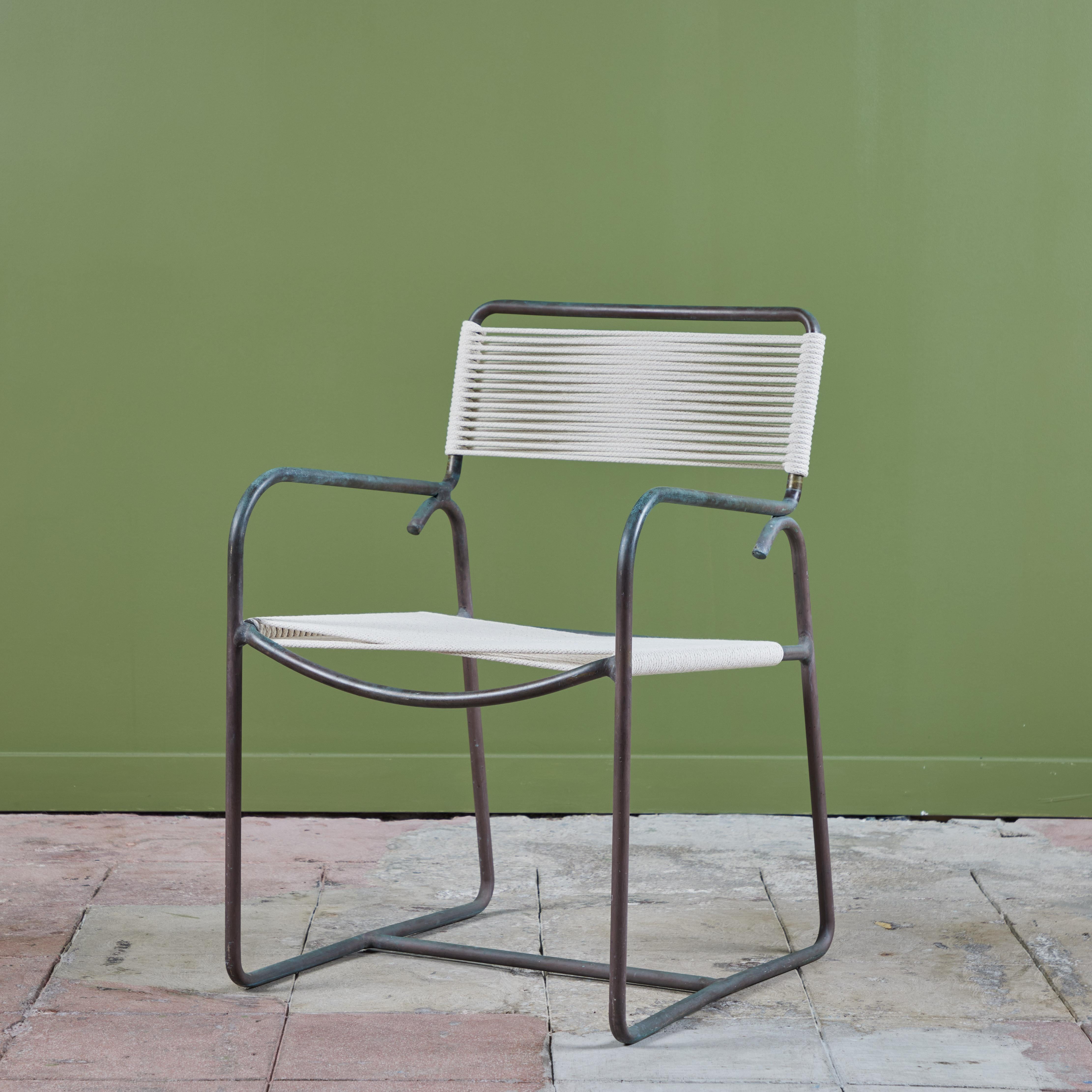 A model C1700A patio armchair in patinated bronze, designed by Walter Lamb and produced by Brown Jordan. The chair has a tubular frame supported by a bent bronze runner and arm on each side. The seat and backrest have been re-strung with a cotton