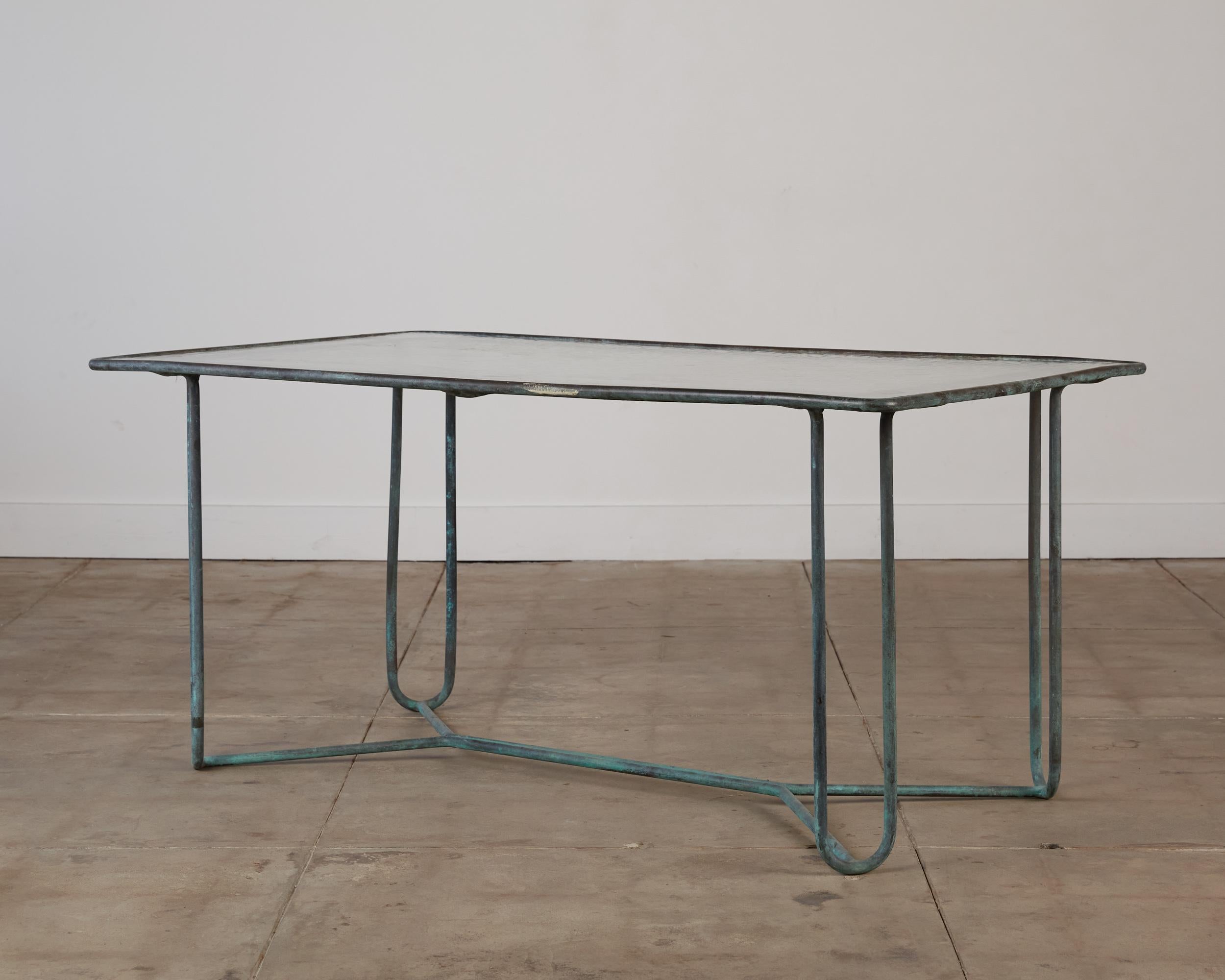 A dining table in patinated bronze designed by Walter Lamb and produced by Brown Jordan. The table has a rectangular shape with rounded corners, supported by four hairpin legs in matching bronze. The legs are joined by diagonal stretchers that sit