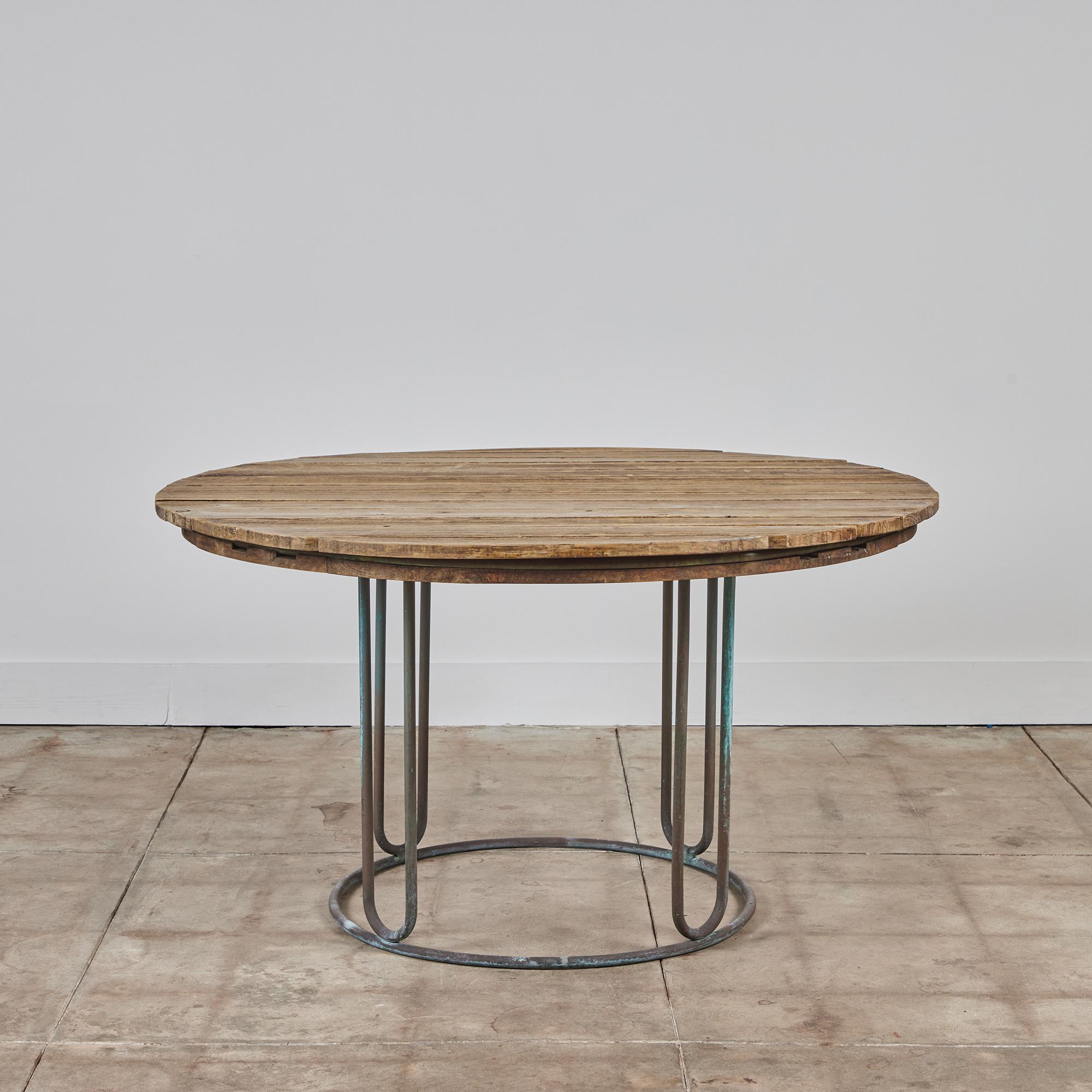 Round patio table designed by Walter Lamb and manufactured by Brown Jordan. The table has a slatted surface in the original weathered wood, mounted on a bronze base. Its subtle geometry suggests an Arts & Crafts sensibility, with radial supports and