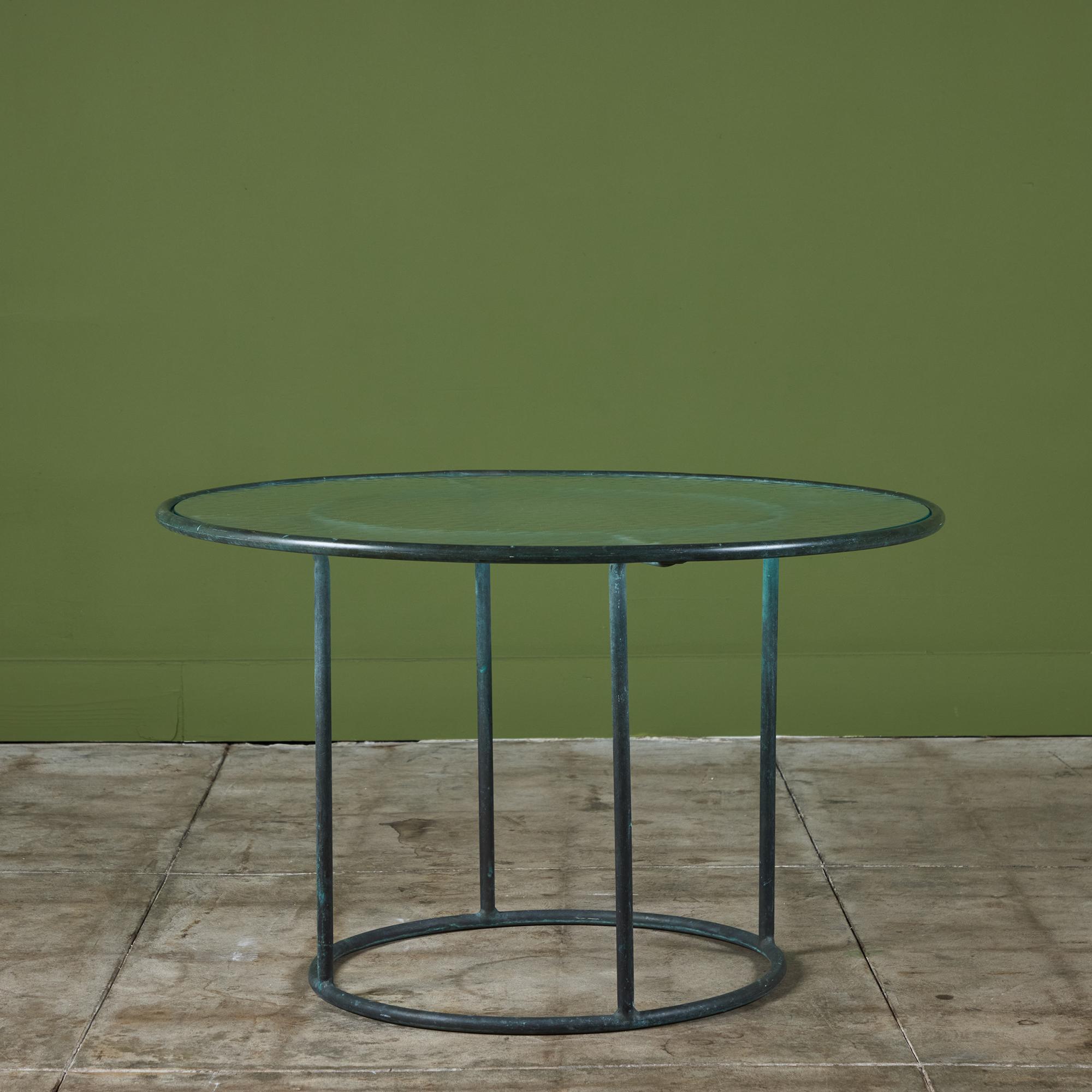 A patio side table in patinated bronze designed by Walter Lamb and produced by Brown Jordan. The frame is described by two concentric rings of bronze with radial supports and a circular bronze base. The round tabletop is a single piece of hammered