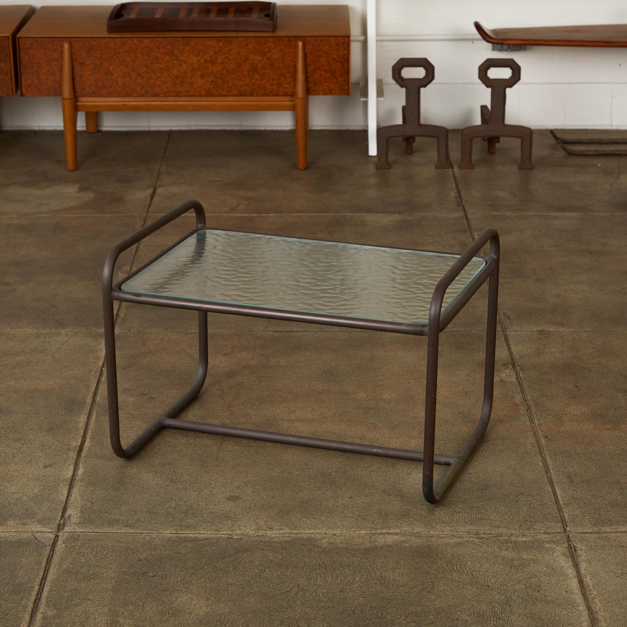 Patio side table designed by Walter Lamb and produced by Brown Jordan. The table frame is bronze tubing with a verdigris patina with an inset hammered glass tabletop. Two curved rails form the legs and create the “handles” on either side of the